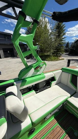 Green and white boat with cushioned seating and modern design, parked in a scenic setting.