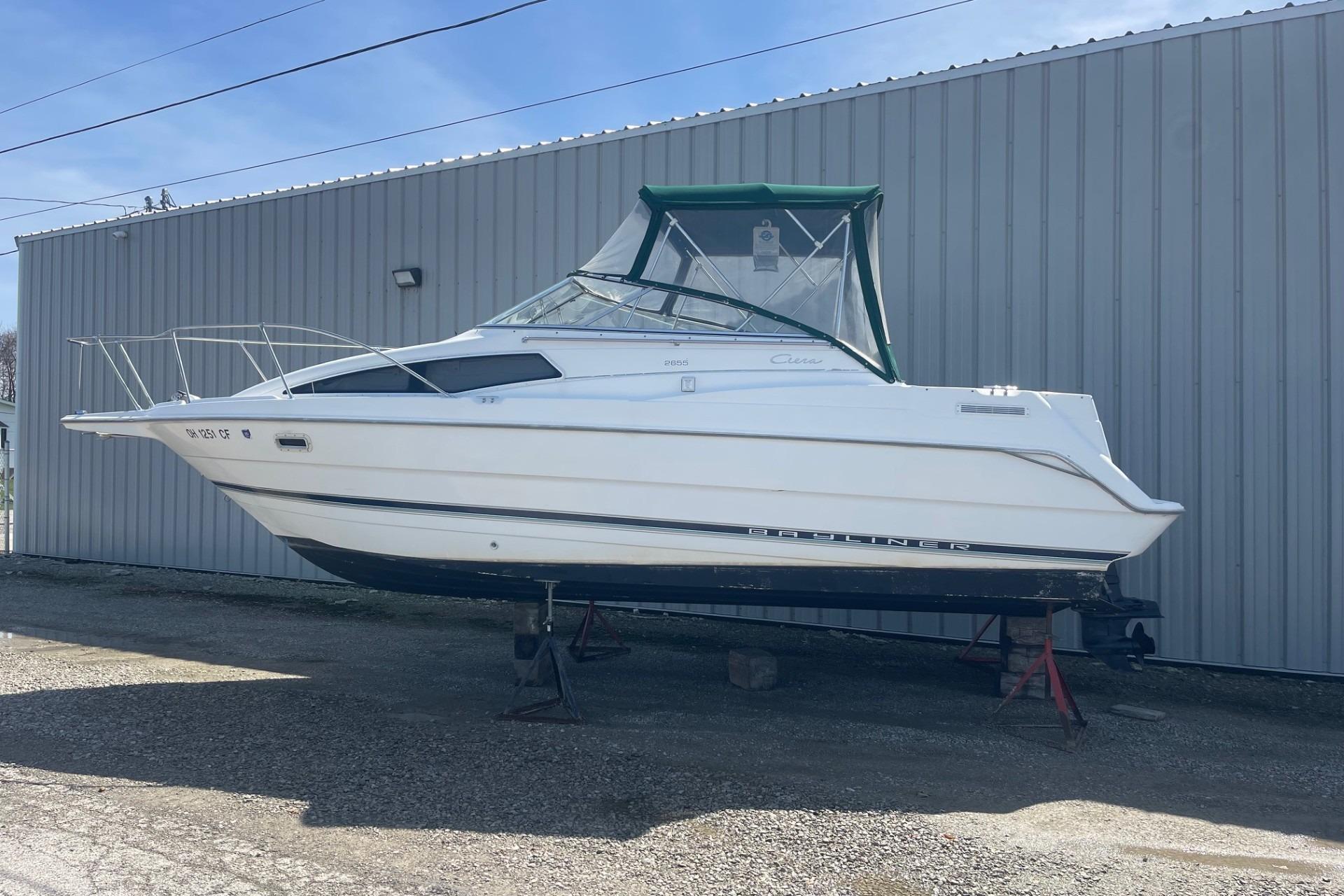 1997 Bayliner 2655 Ciera boat on stands, white hull, green canopy, parked by metal building.