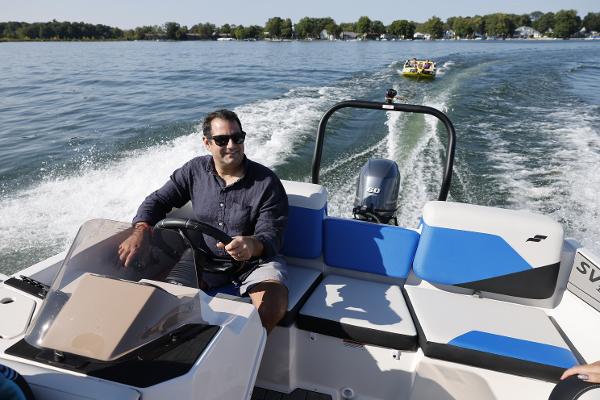 Man driving 2025 Starcraft SV 16 OB boat on a lake, towing a yellow inflatable.