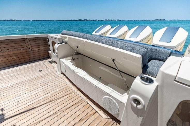 2026 Scout 670 LXS boat with open storage compartment, wooden deck, and ocean backdrop.