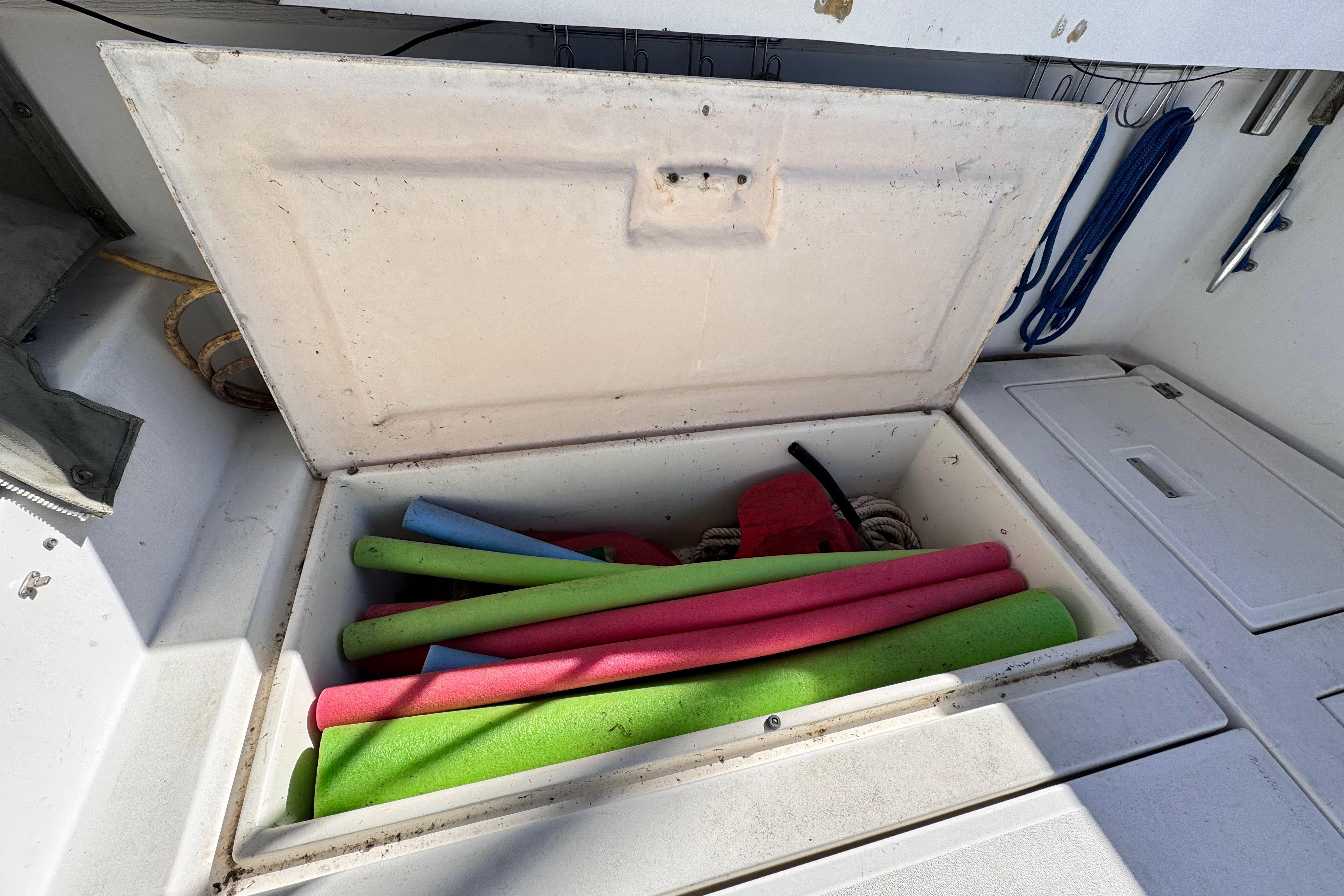 Open storage compartment on 1987 Luhrs Alura 30 boat with colorful pool noodles.