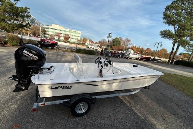 2025 Mako Pro Skiff 17 CC boat on trailer, parked outdoors with trees and buildings in background.