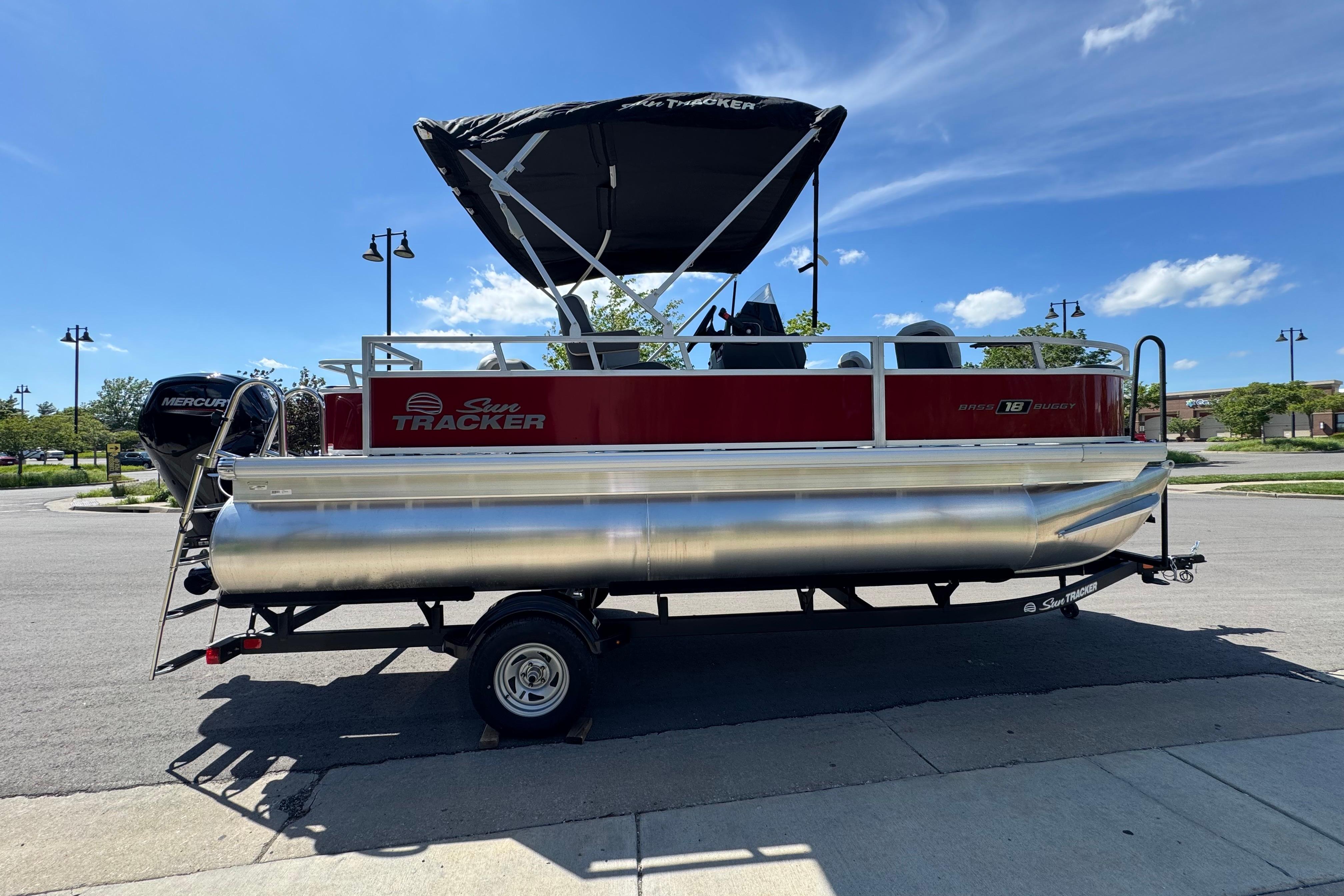 2026 Sun Tracker Bass Buggy 18 DLX pontoon boat with canopy on trailer, parked outdoors.