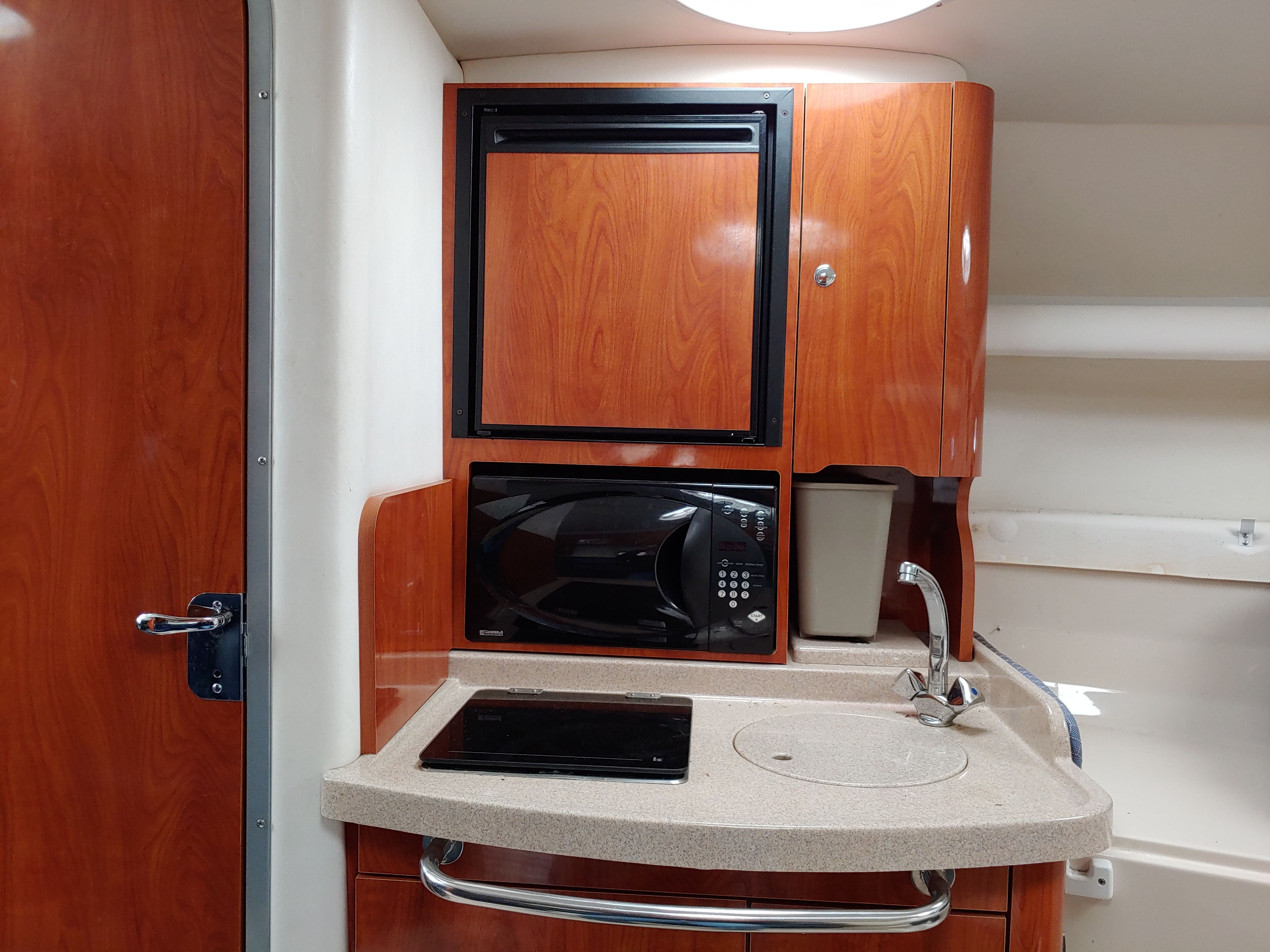 Compact boat kitchenette with wooden cabinets, microwave, and sink.