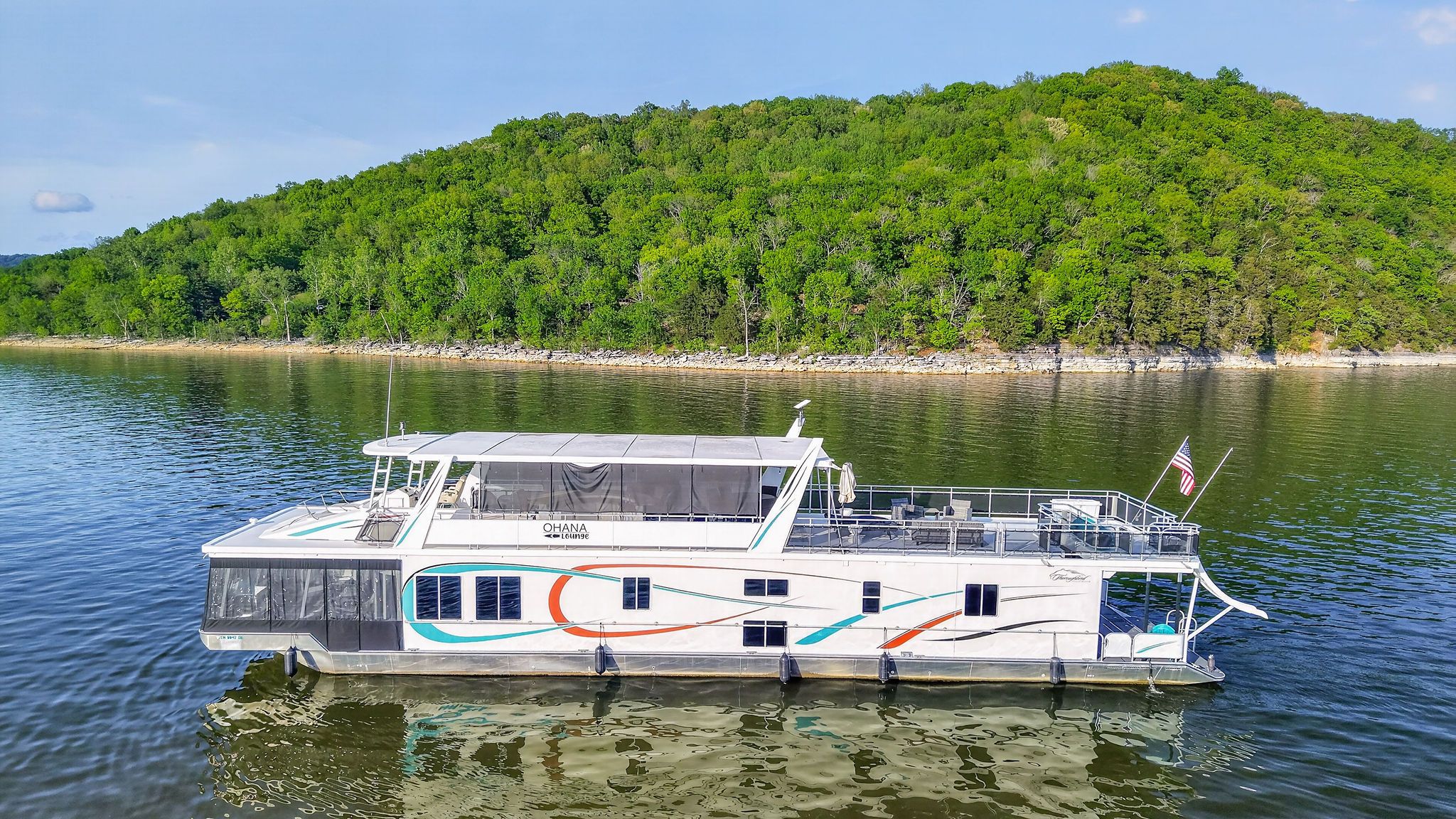 Houseboat on calm lake with wooded hill, 2010 model.