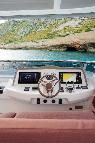 2025 Lagoon SIXTY 7 yacht helm with dual screens, steering wheel, and scenic coastal view.