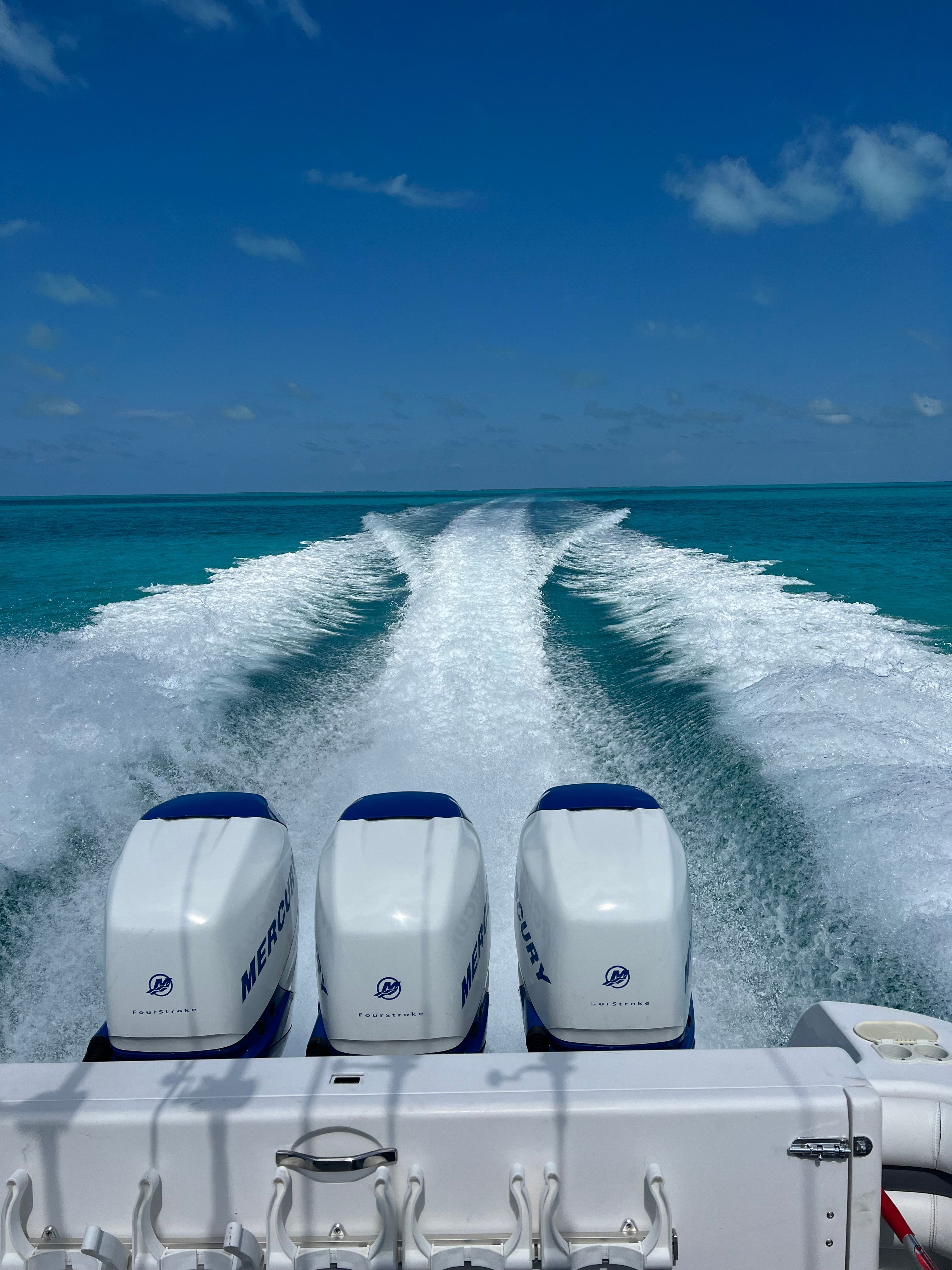 Three Mercury outboard engines power a boat across turquoise water, leaving a white wake.