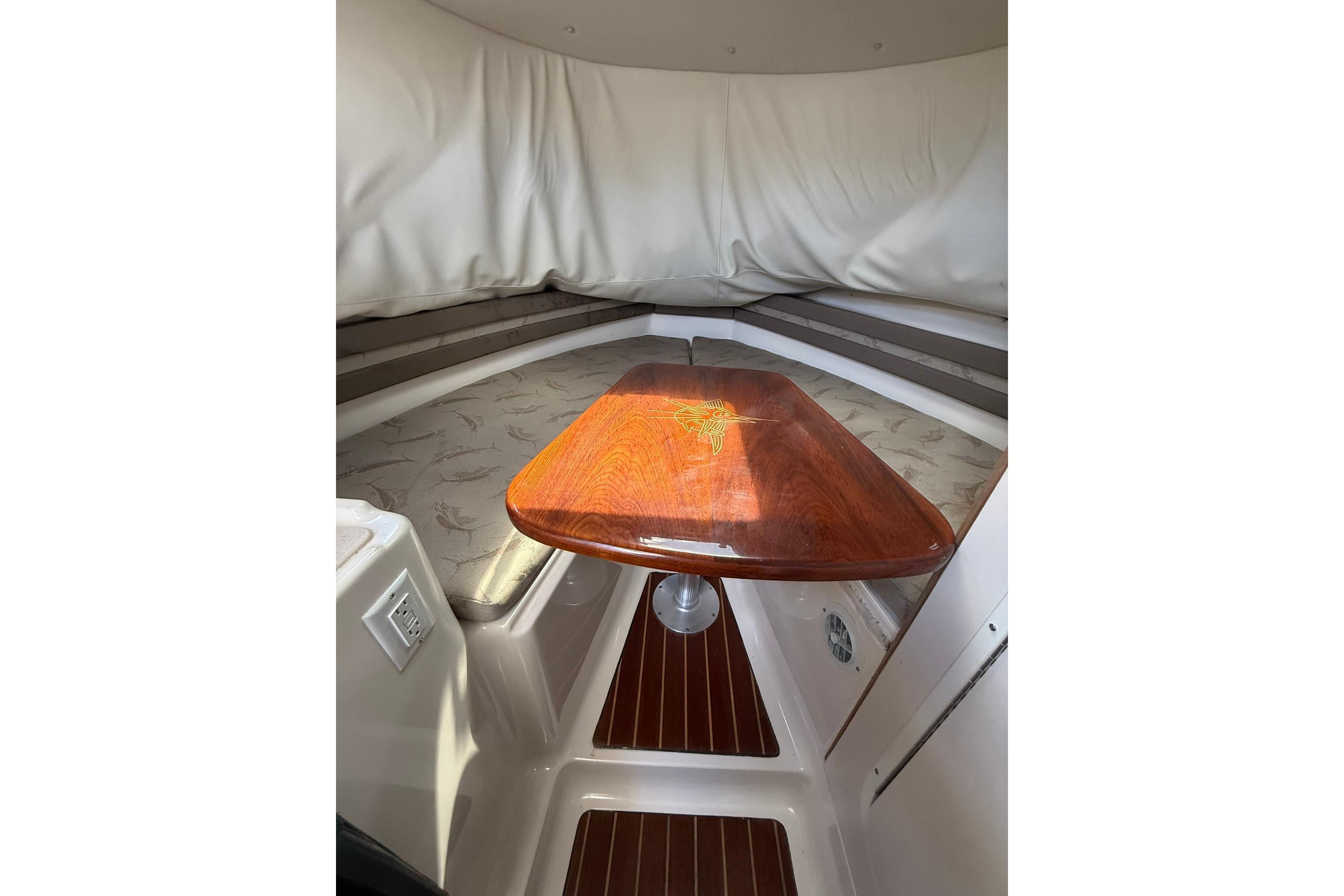 2003 Pursuit 2870 Walkaround cabin interior with wooden table and cushioned seating.