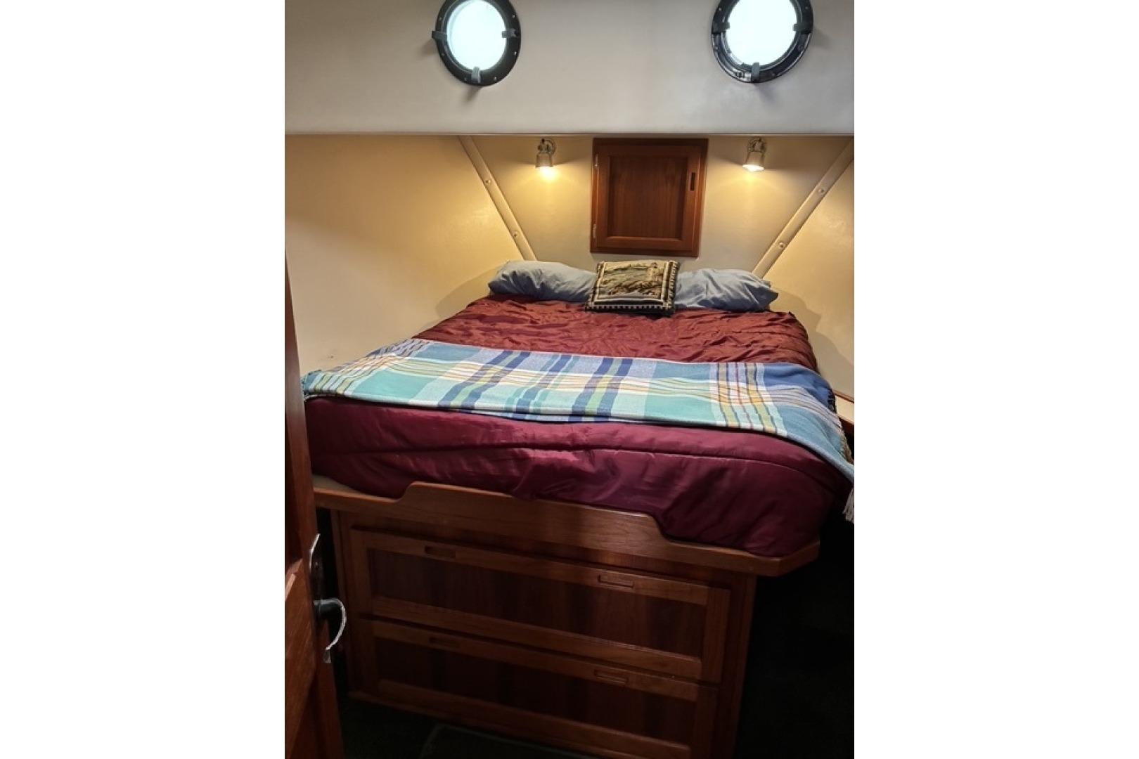 Cozy cabin bedroom in a 2000 Nordic Tug 37 with portholes and warm lighting.