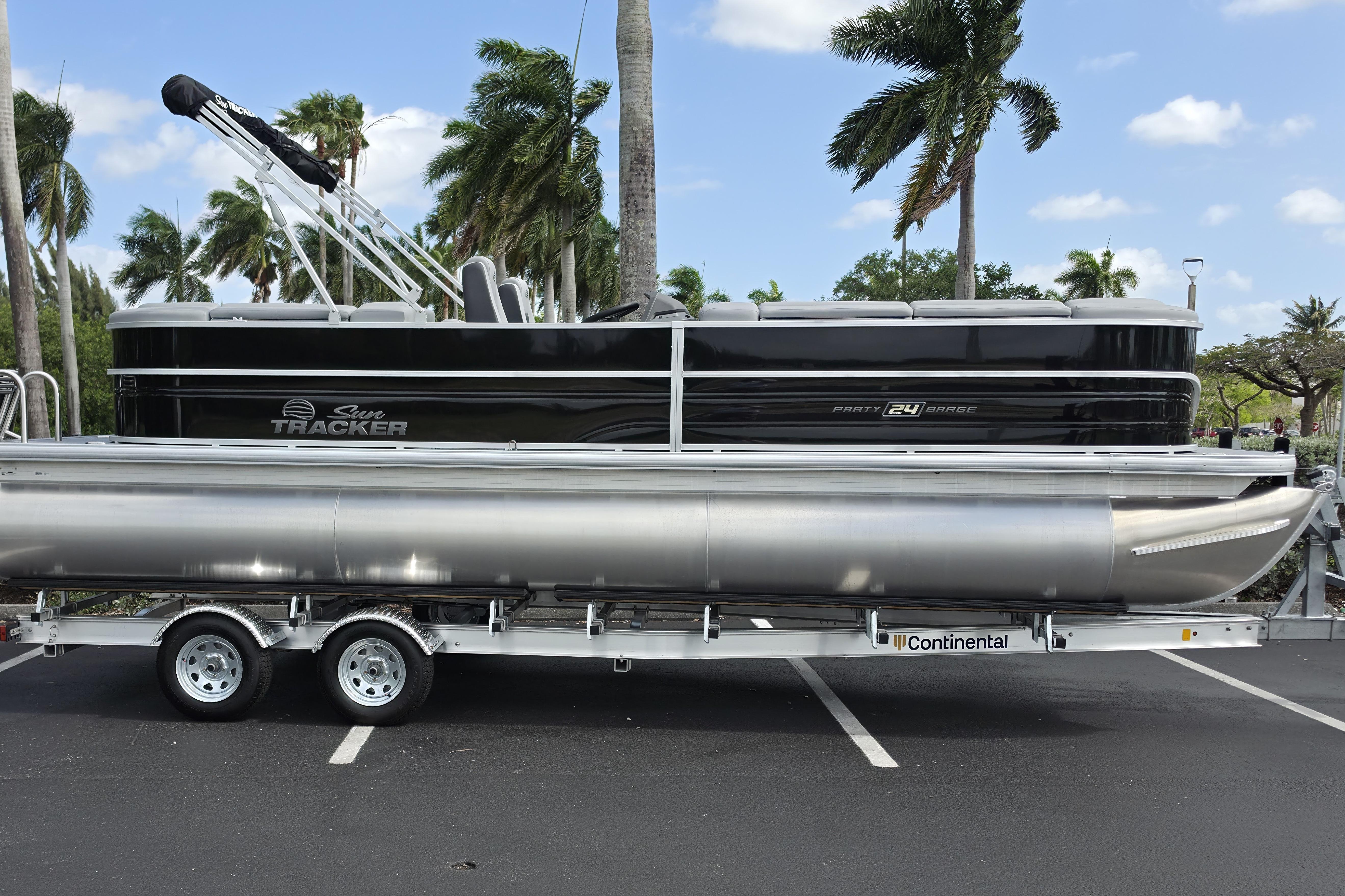 2026 Sun Tracker Party Barge 24 XP3 pontoon boat on trailer, parked with palm trees.
