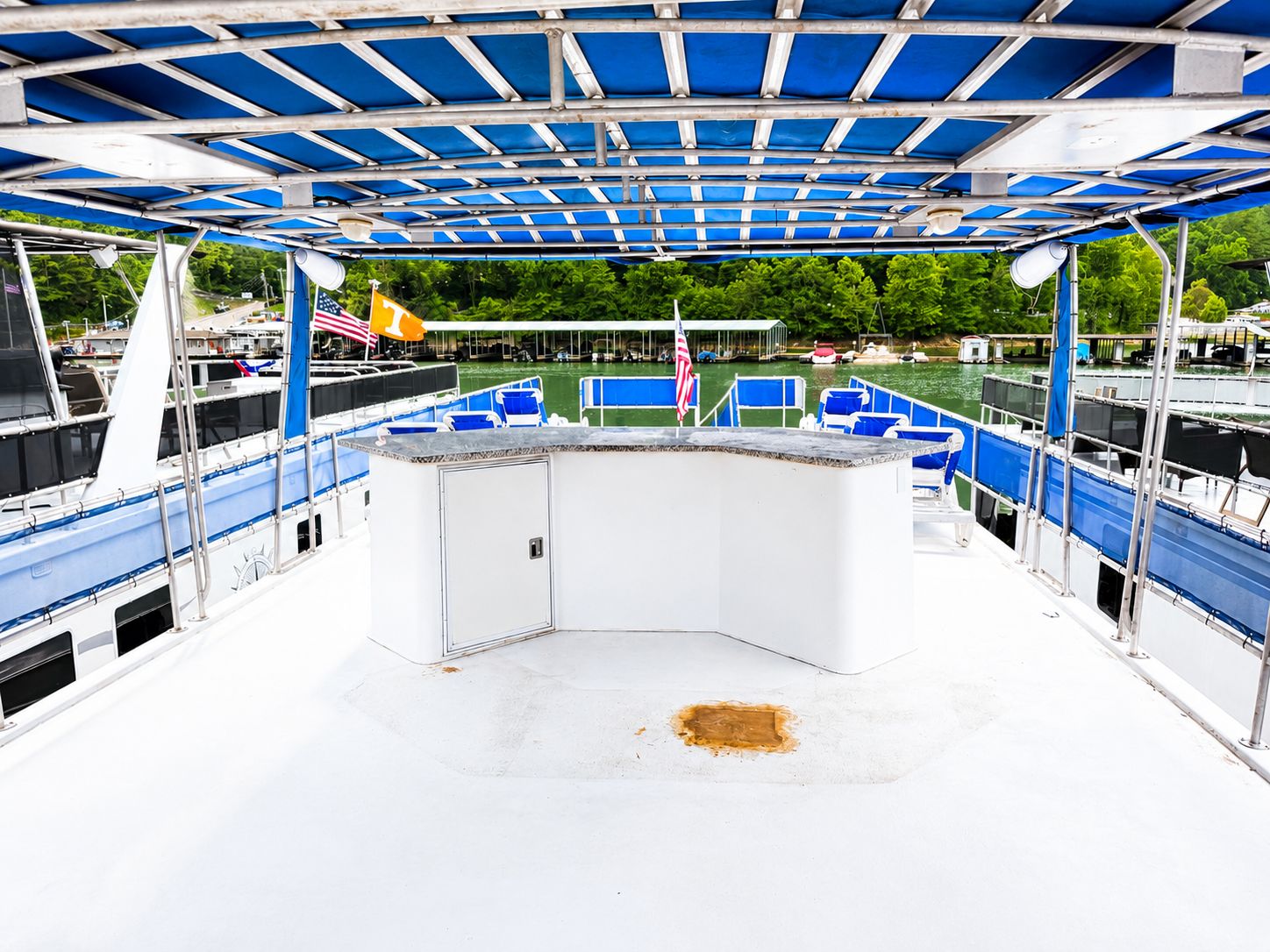 The top deck of a houseboat with a bar and seating area under a blue canopy.