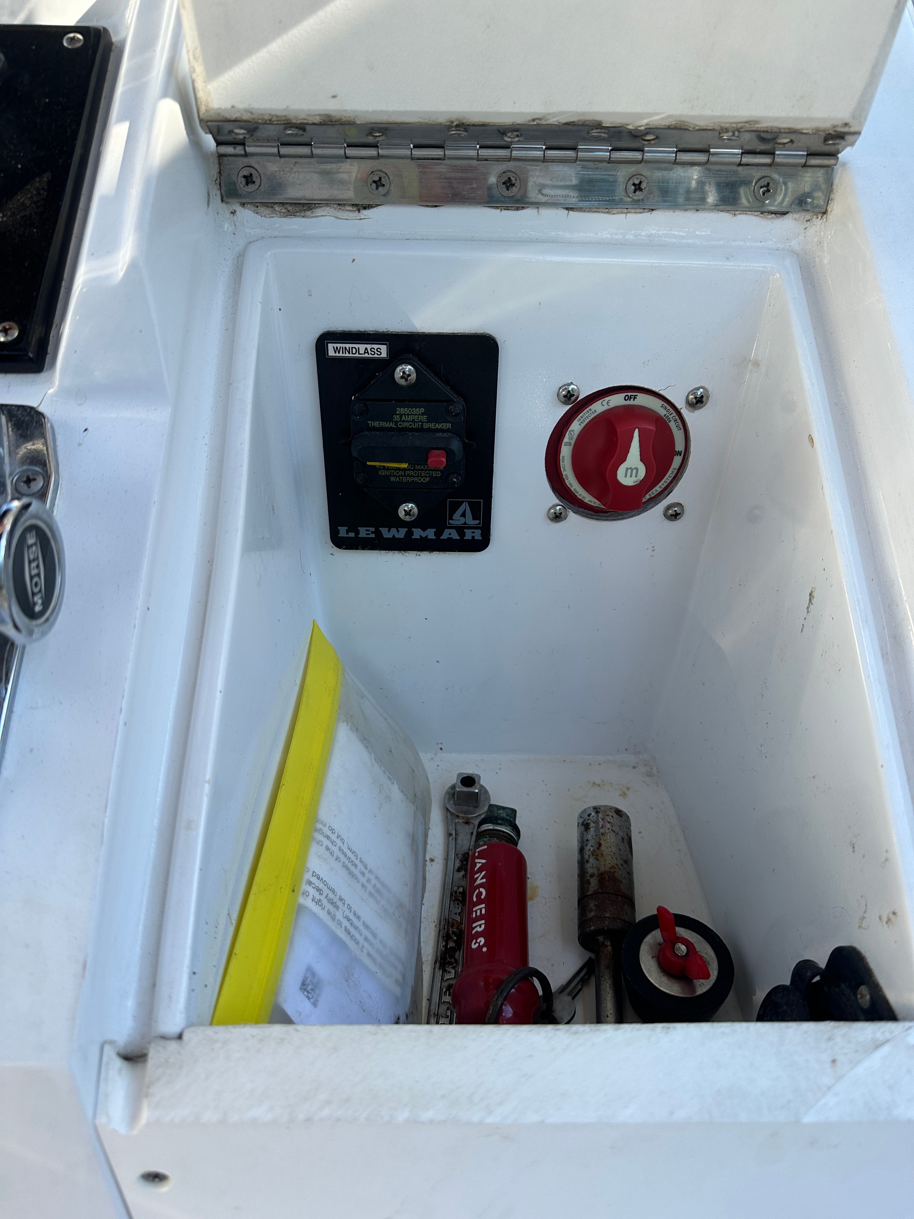 An open storage compartment on a boat with a fire extinguisher, a switch, and a lever.