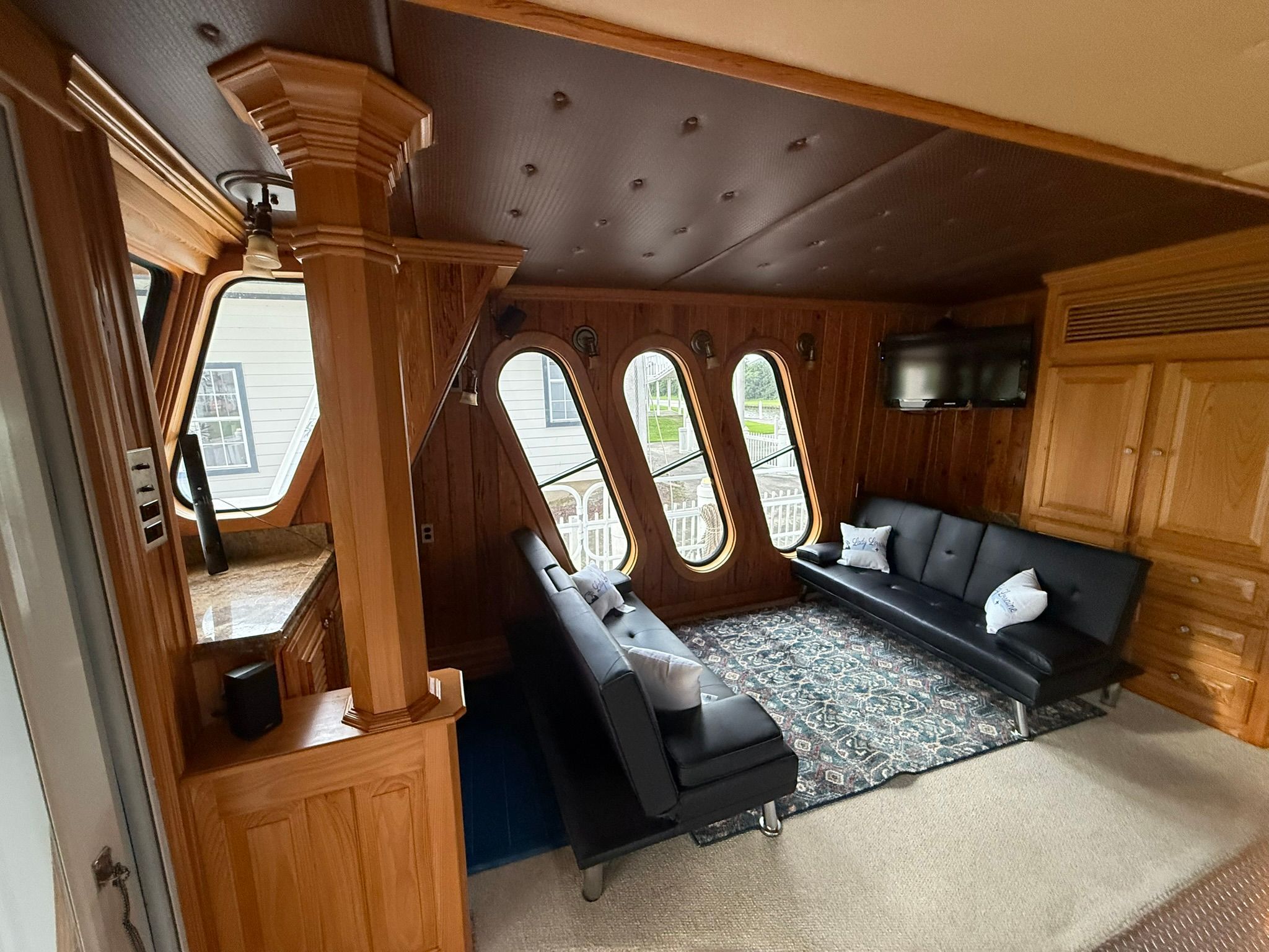 Interior of a boat with wooden walls, black sofas, and oval windows.