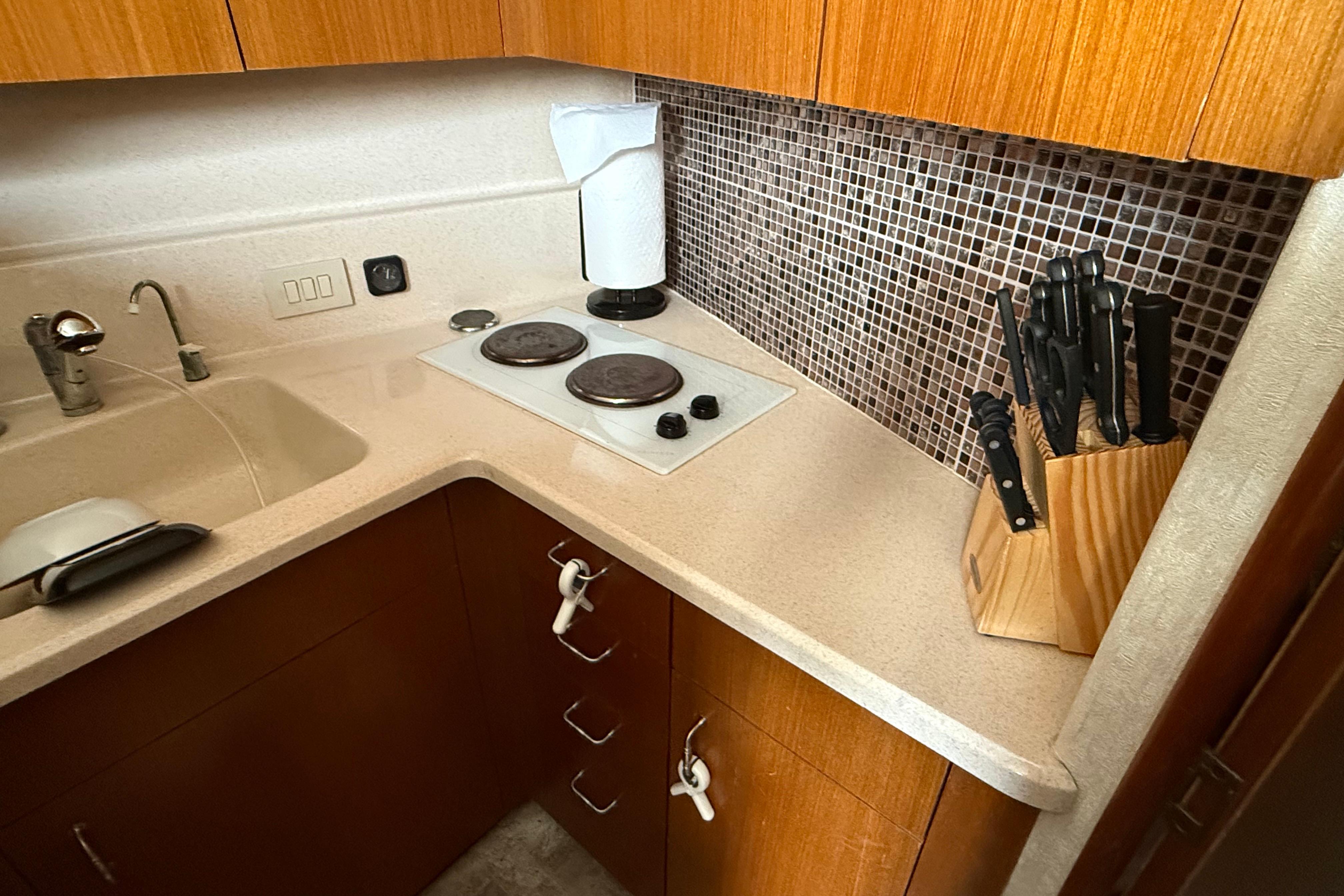 Compact kitchen in 1999 Ocean Yachts 40 Express, featuring stove, sink, and knife set.