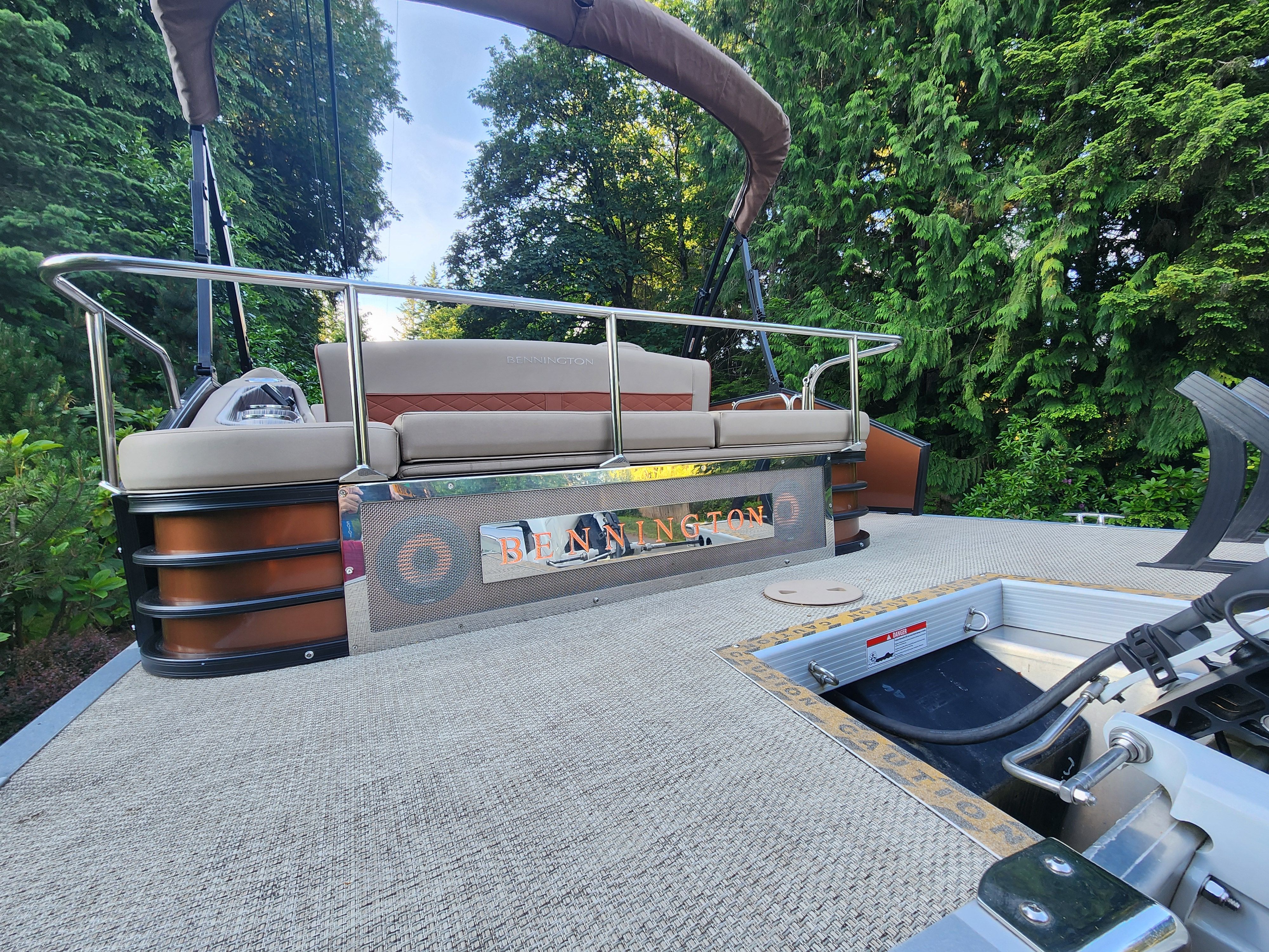 Bennington 22 LSB pontoon boat with beige upholstery and stainless steel railing, surrounded by lush greenery.