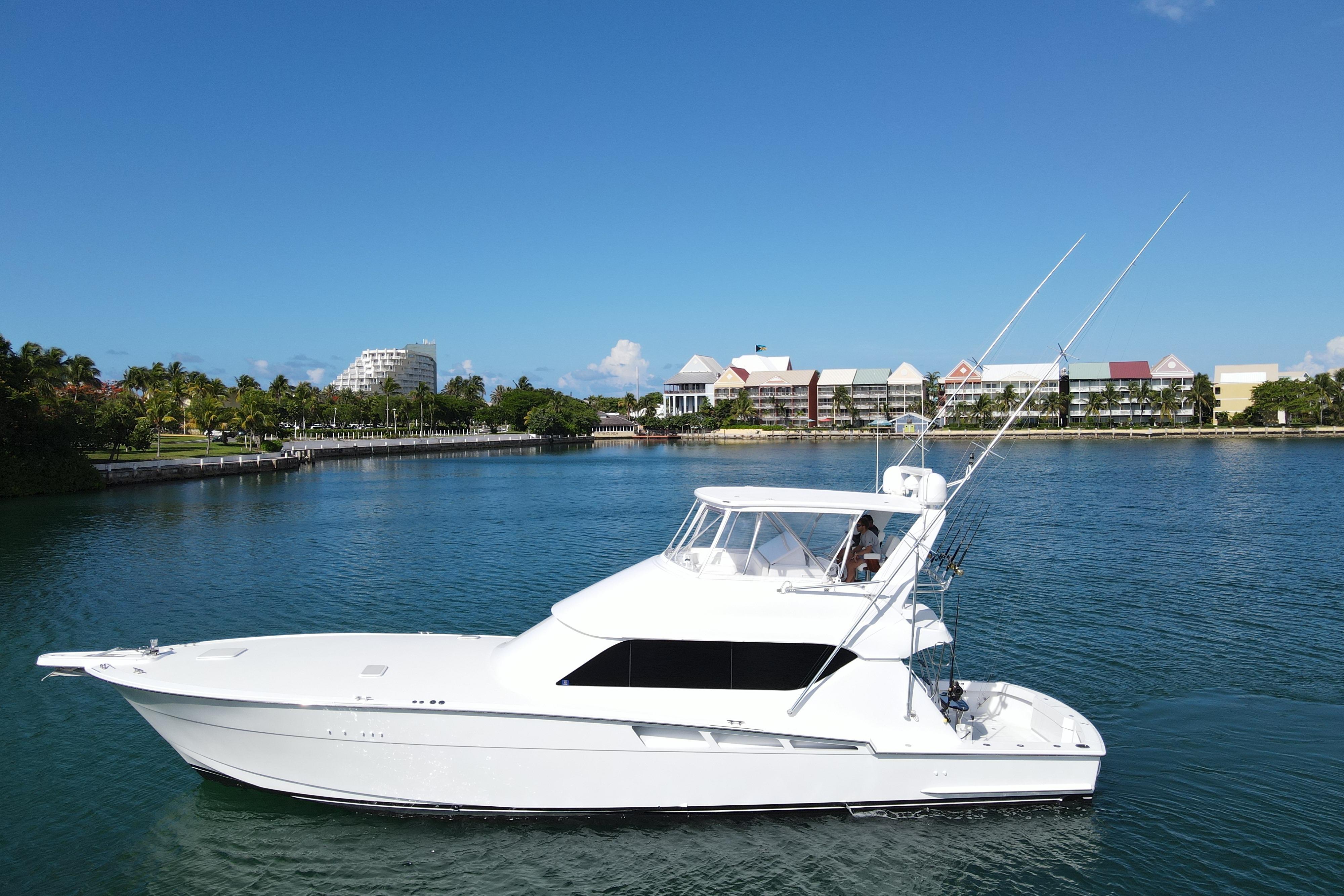 2004 Hatteras 60 Convertible yacht cruising on a sunny day near waterfront buildings.