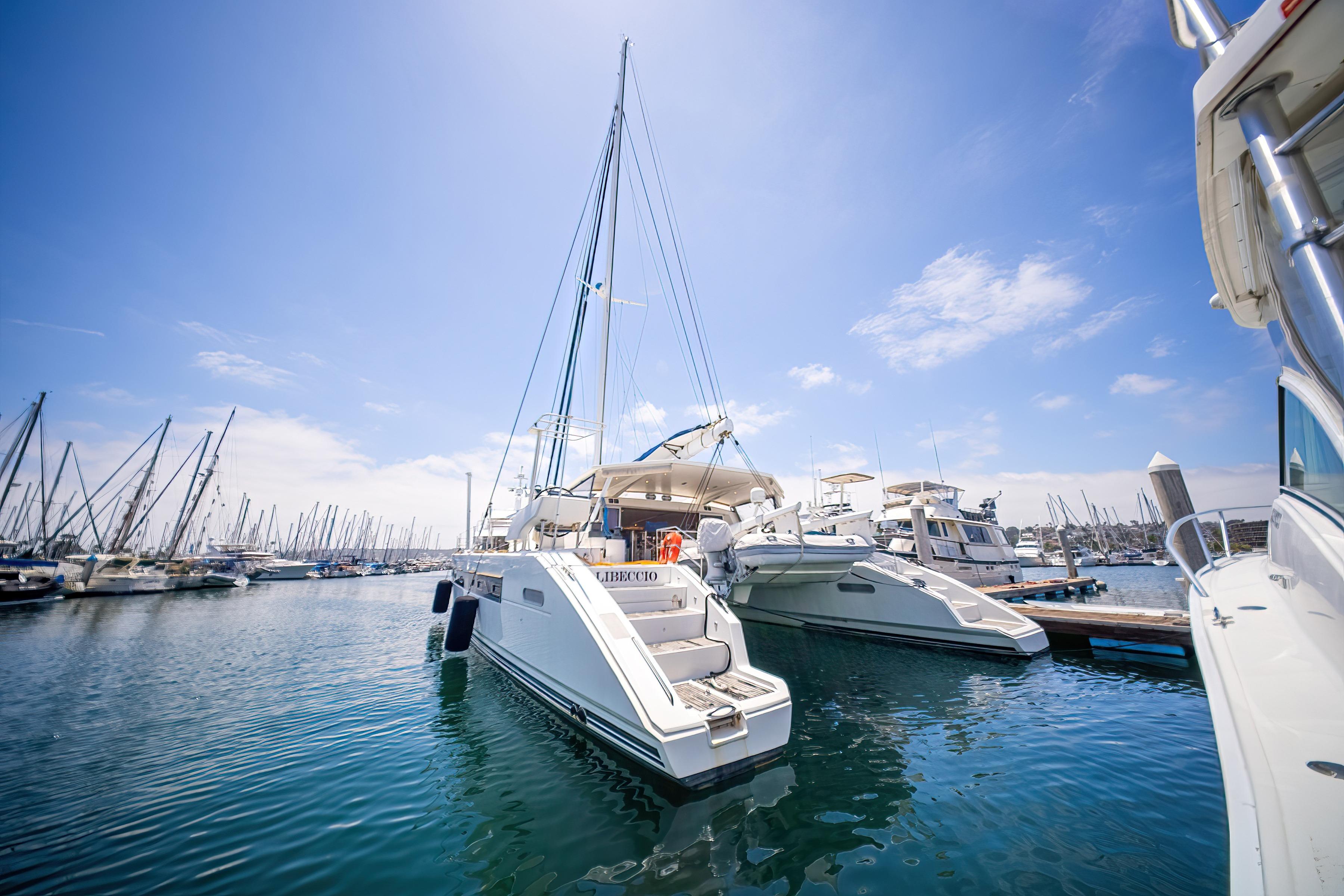 Catana 65 catamaran from 2009 docked in a sunny marina, surrounded by other boats.