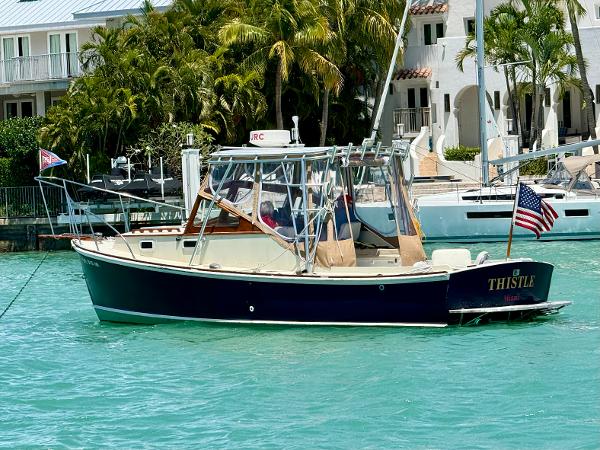 1978 Dyer 29 Trunk Cabin boat named "Thistle" on turquoise water near waterfront homes.