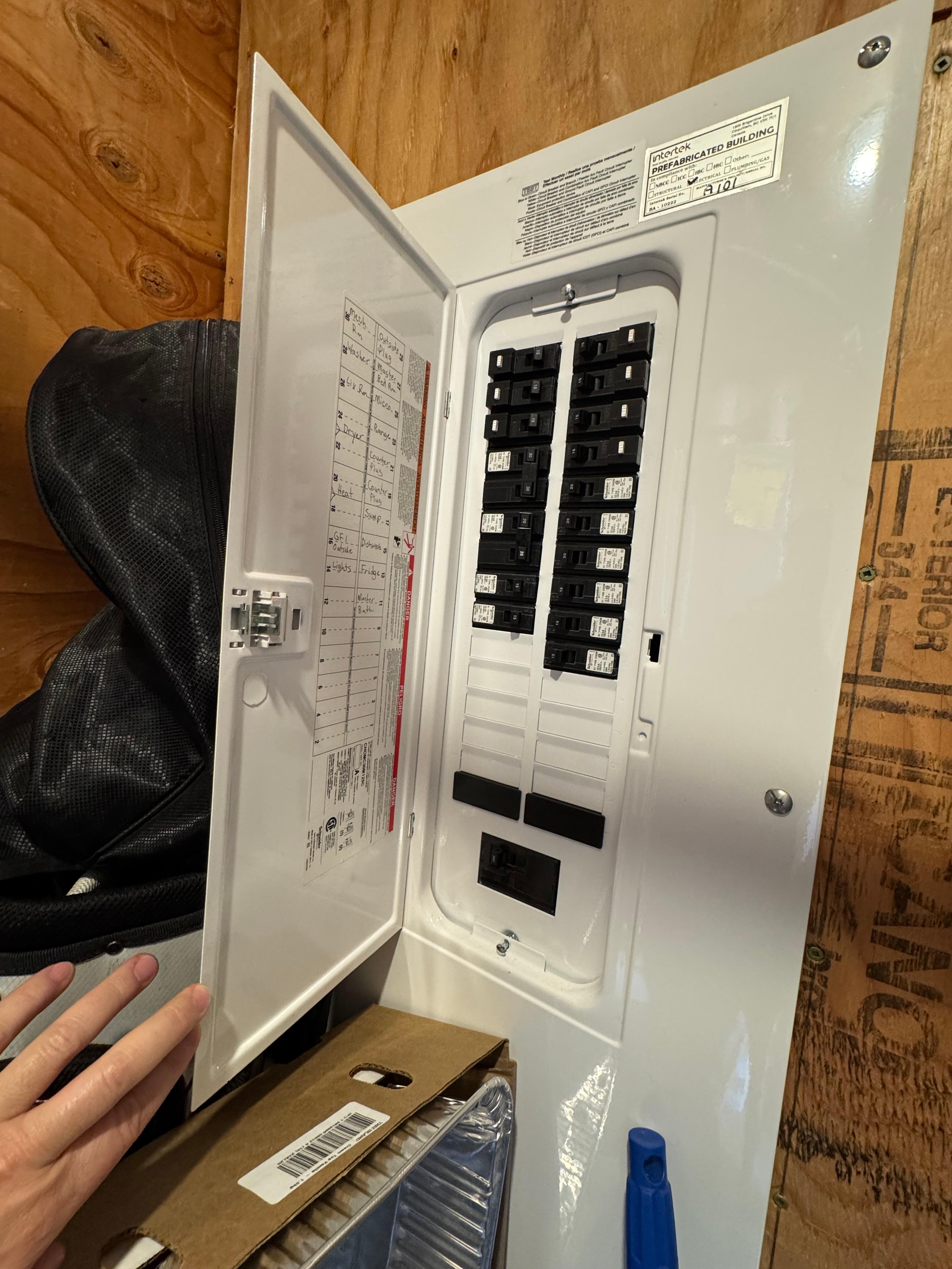 Electrical panel with open door showing circuit breakers in a wooden room.
