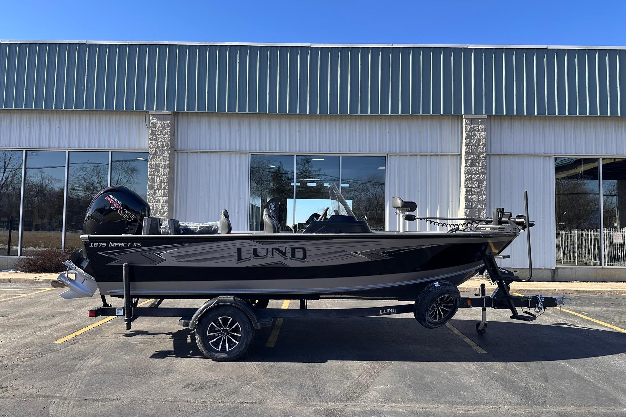 2026 Lund 1875 Impact XS SS boat on trailer, parked outside a building.
