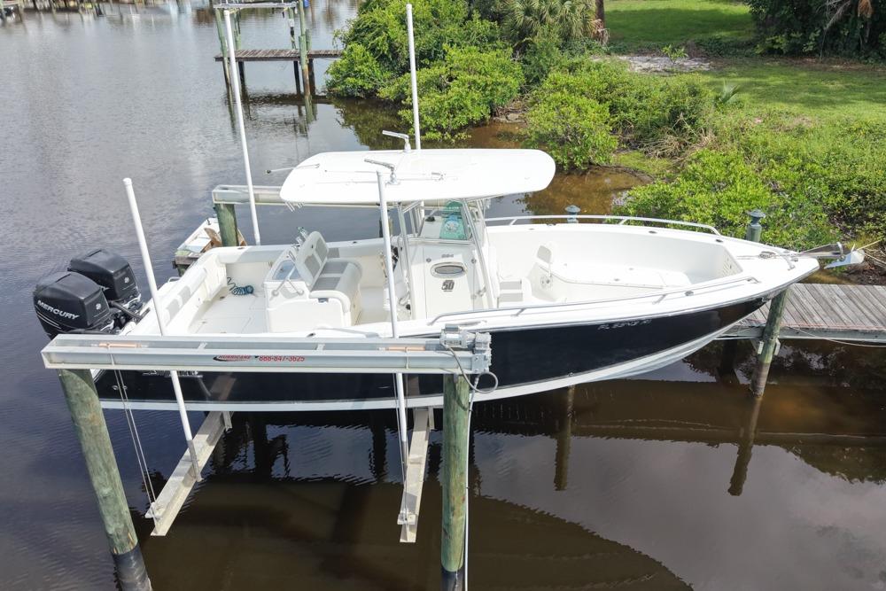 2018 Mako 284 Center Console boat on lift, docked by lush greenery.
