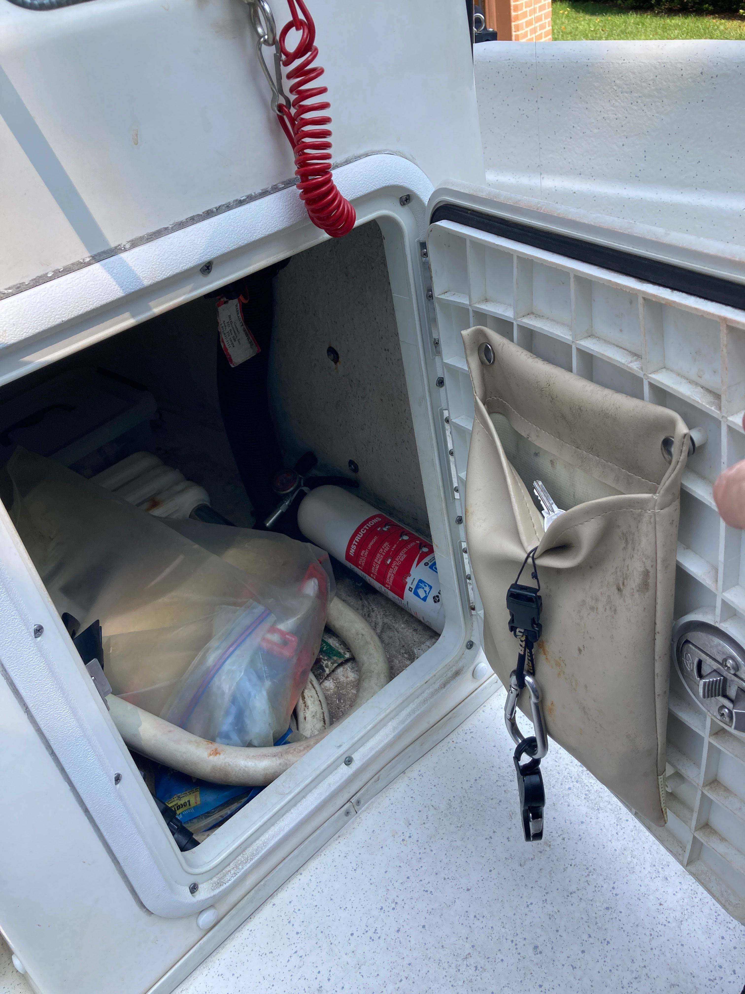 An open storage compartment on a boat with a fire extinguisher and other items.