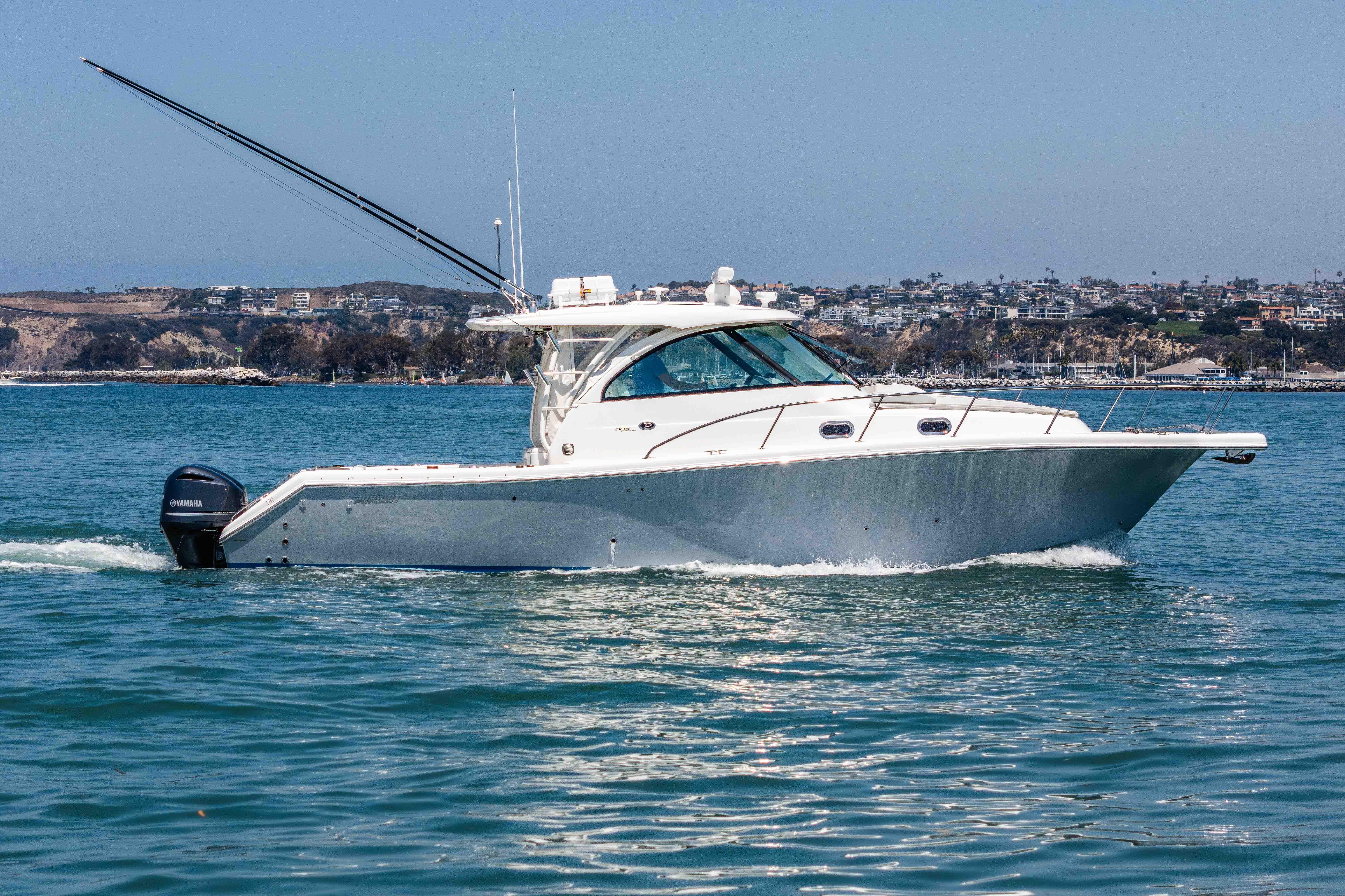2022 Pursuit OS 385 Offshore boat cruising on calm waters near a coastal city.