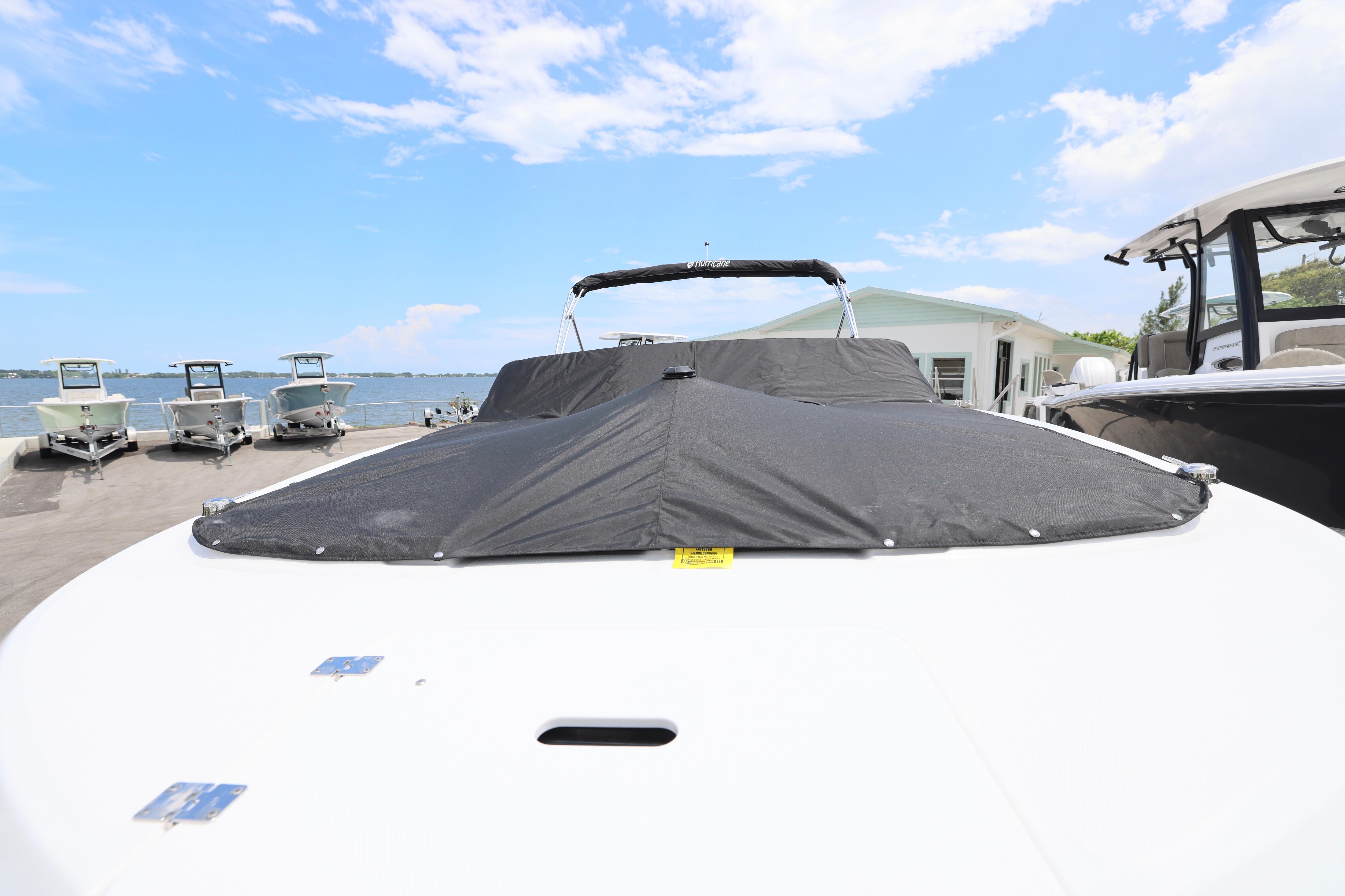 2026 Hurricane SunDeck 2050 OB boat with cover, docked near other boats under a blue sky.
