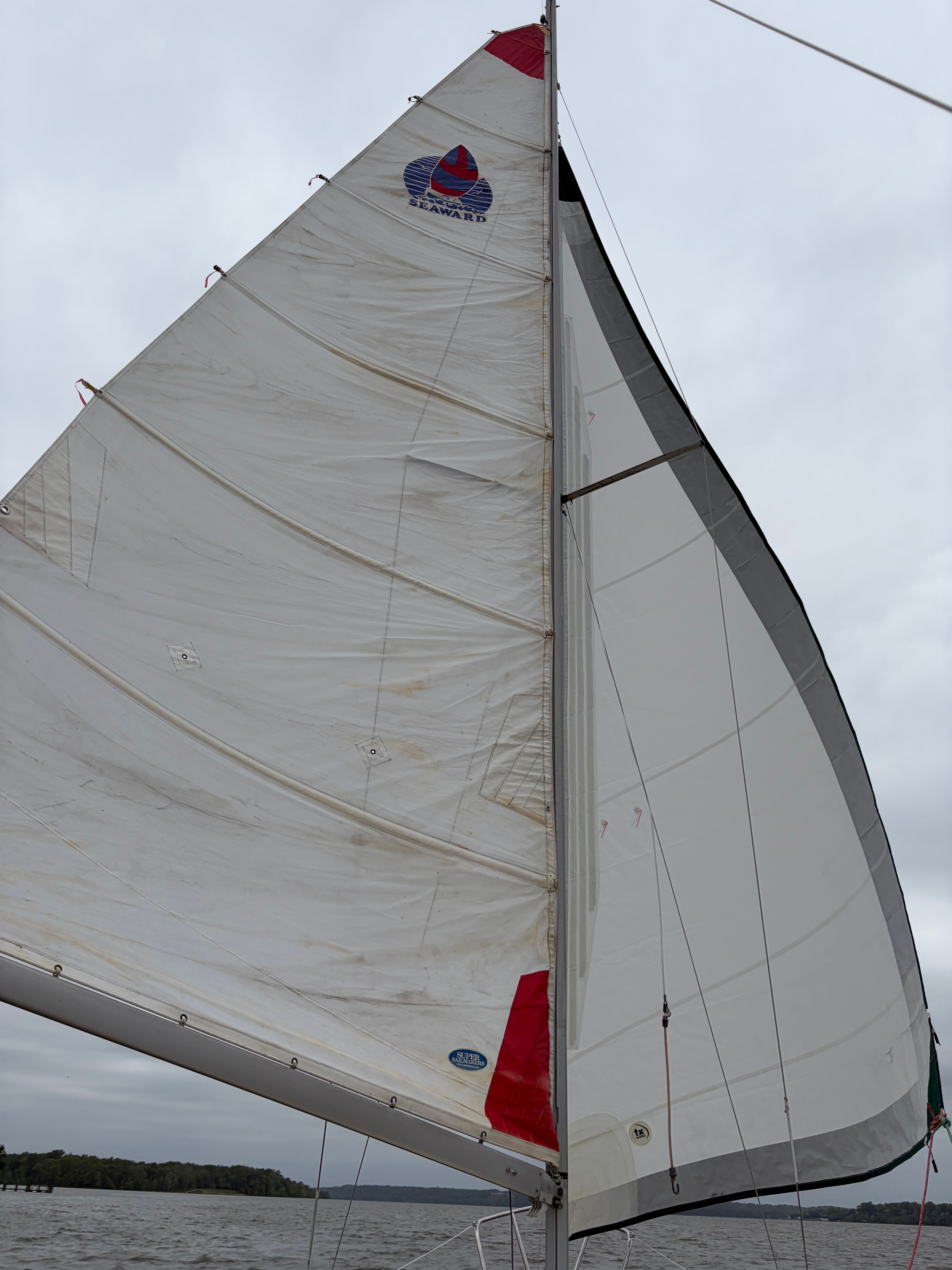 Sailboat with white sails on gray water.