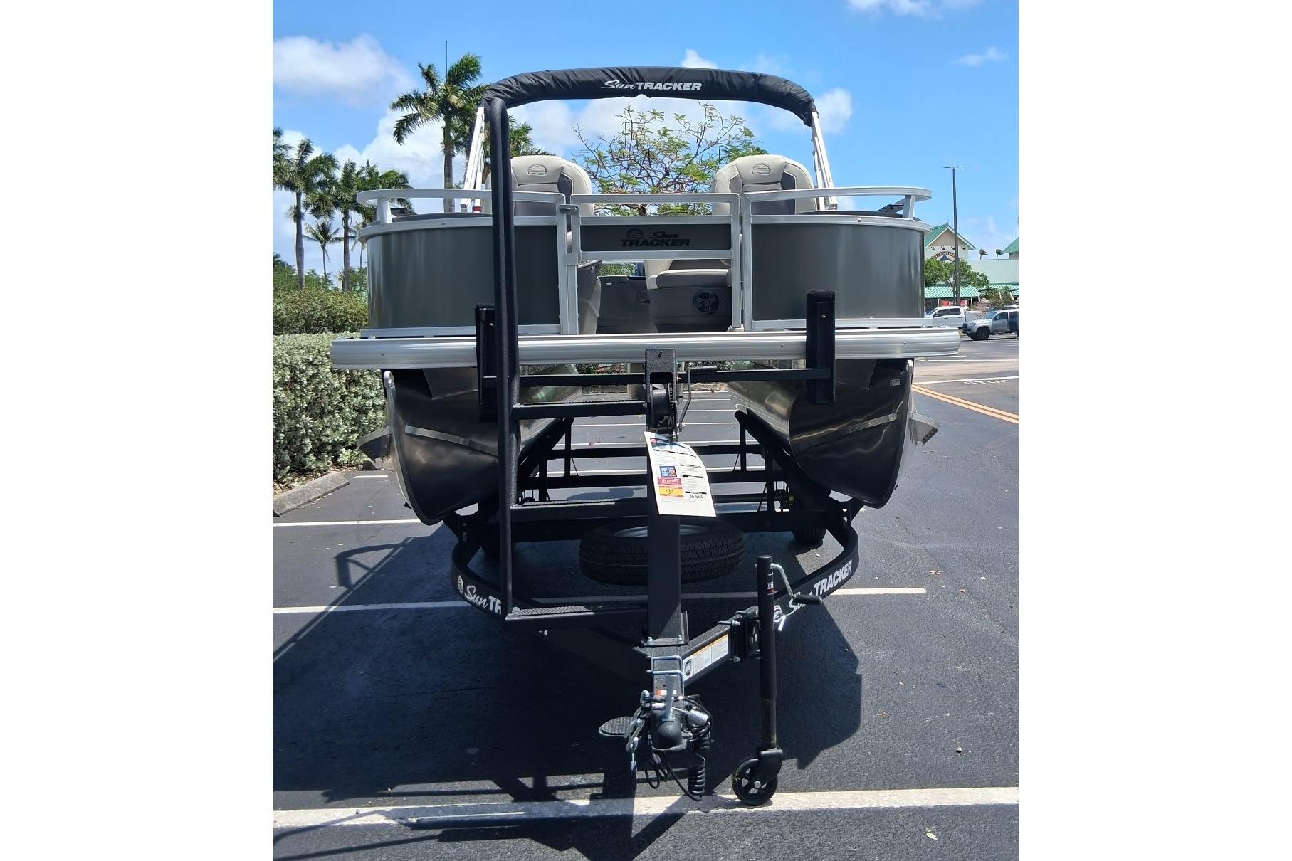 2026 Sun Tracker Bass Buggy 18 DLX pontoon boat on trailer in parking lot.