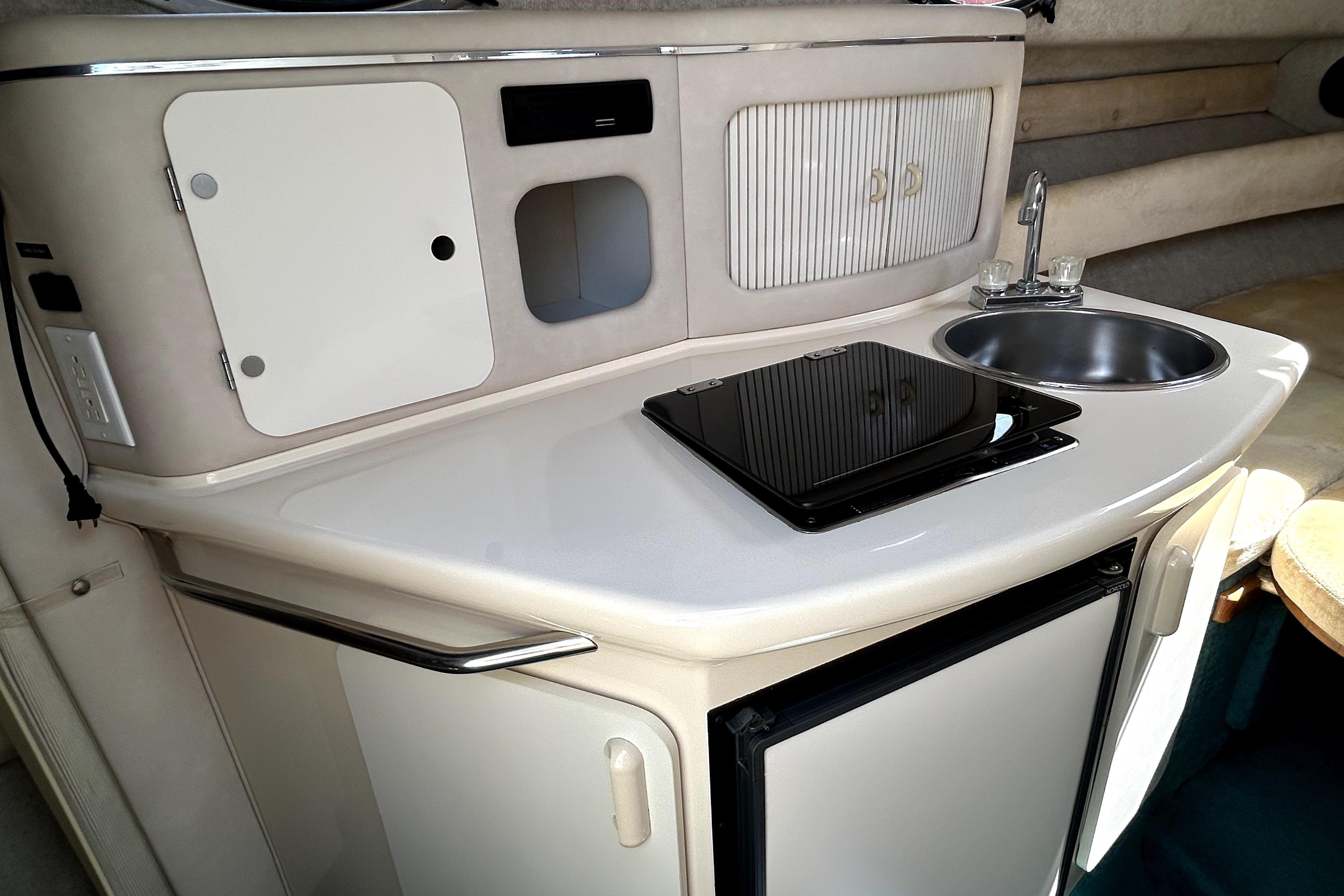 1995 Sea Ray 250 Sundancer boat kitchenette with sink, stove, and storage cabinets.