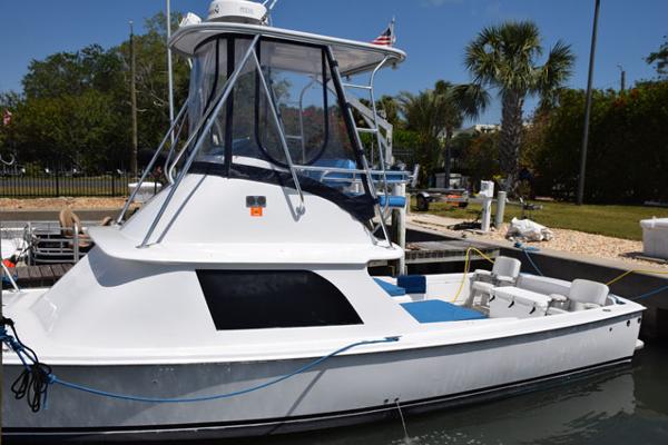 1976 Bertram Flybridge Cruiser docked, featuring sleek design and spacious deck under clear blue sky.