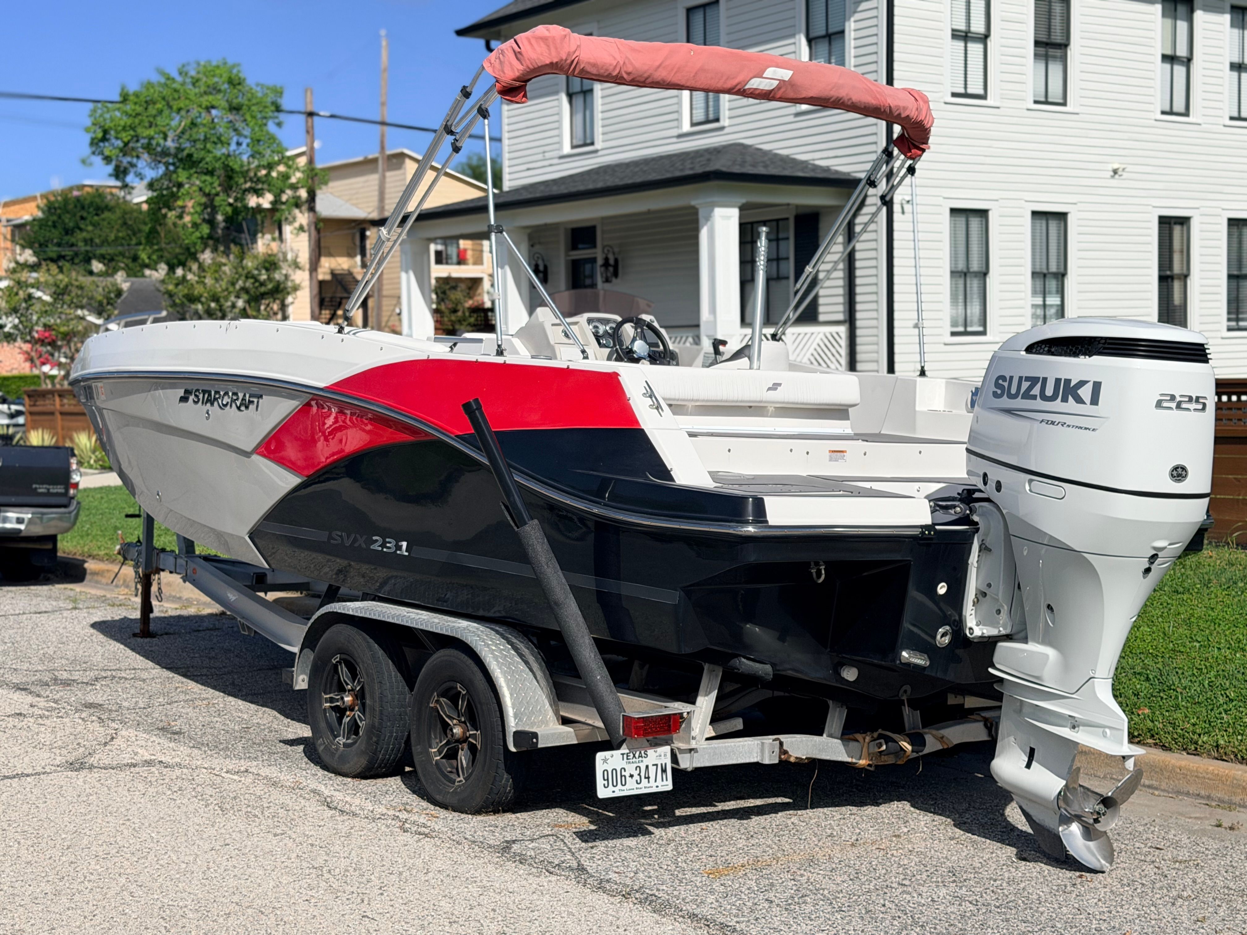 A Starcraft SVX 231 boat on a trailer, parked on a street in front of a house.