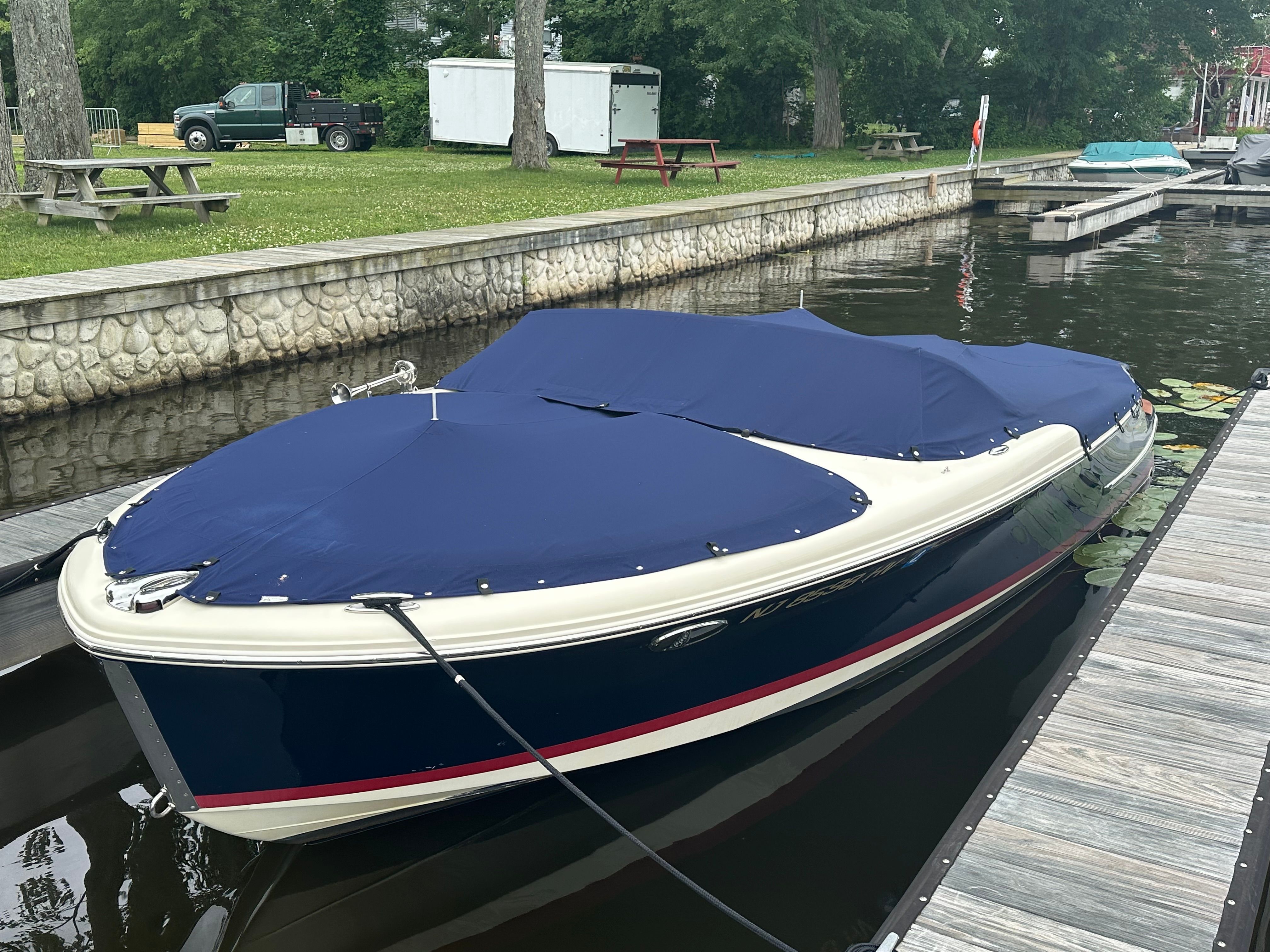A 2014 Chris-Craft Carina 21 docked at a wooden pier, covered with a blue tarp.
