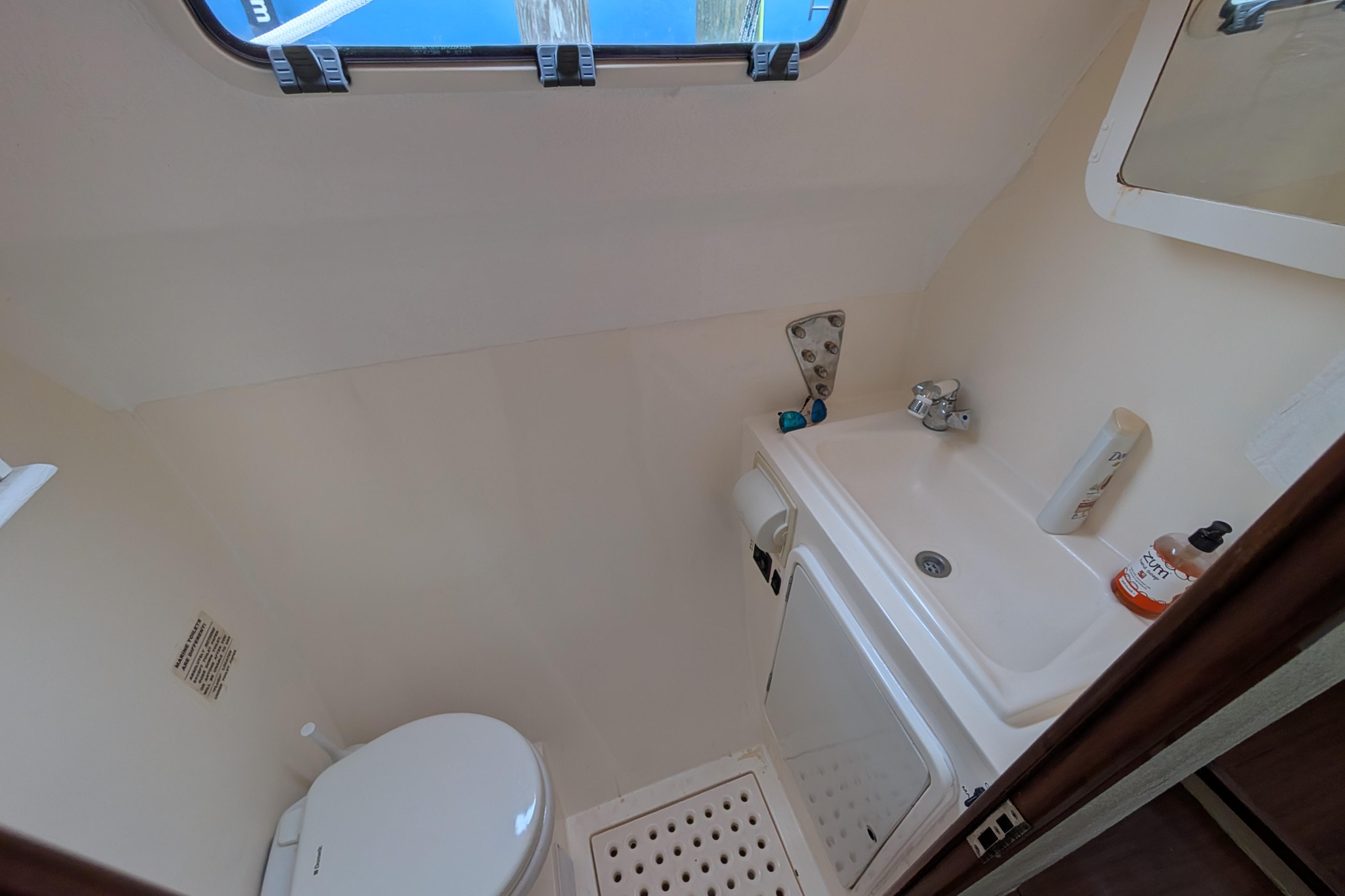 Compact bathroom in a 1999 Island Spirit 37 yacht, featuring a toilet, sink, and window.