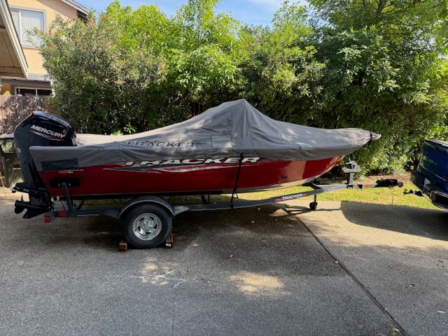 A red Tracker boat, model PGV16WT 16, on a trailer, covered with a protective cover.