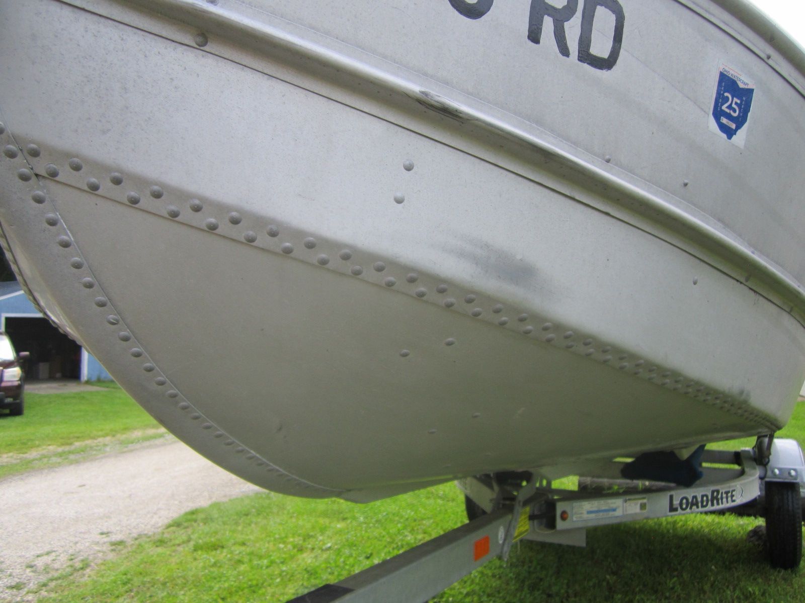 A boat on a trailer, parked on a green lawn.