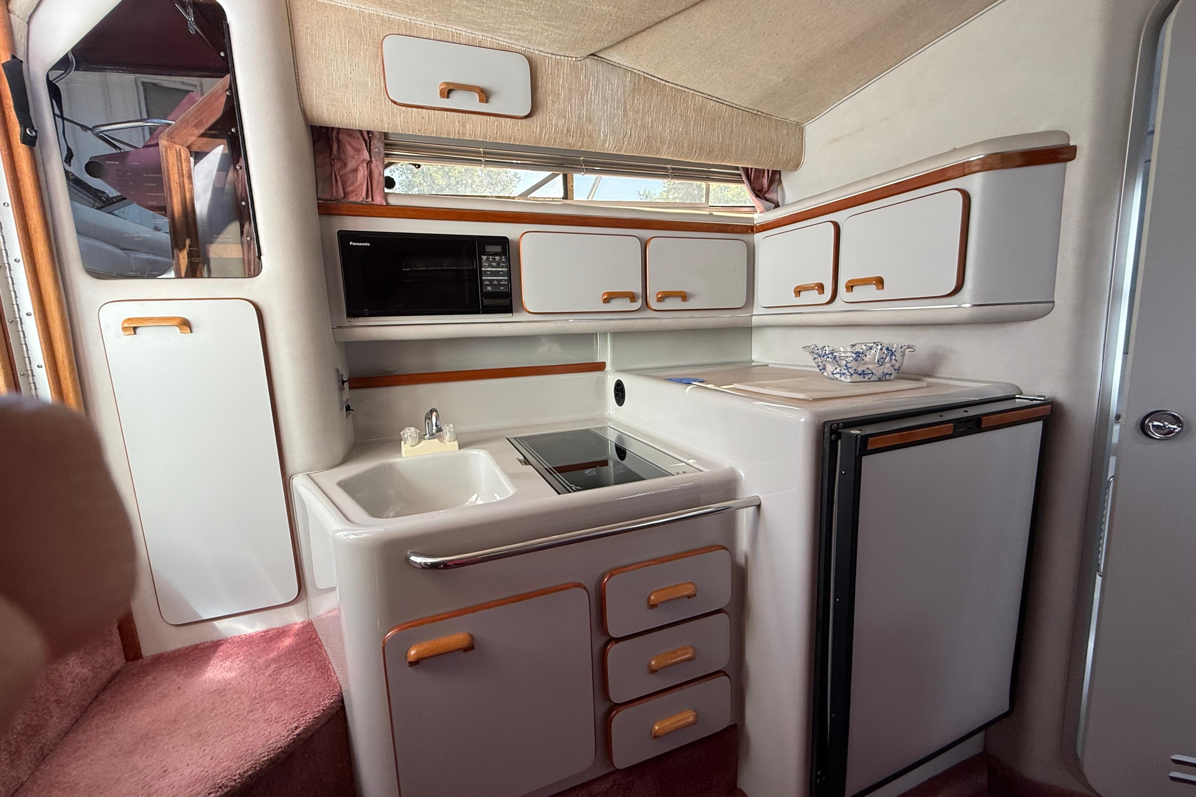 Interior of 1990 Sea Ray 310 Express Cruiser with kitchenette, featuring sink, microwave, and storage cabinets.