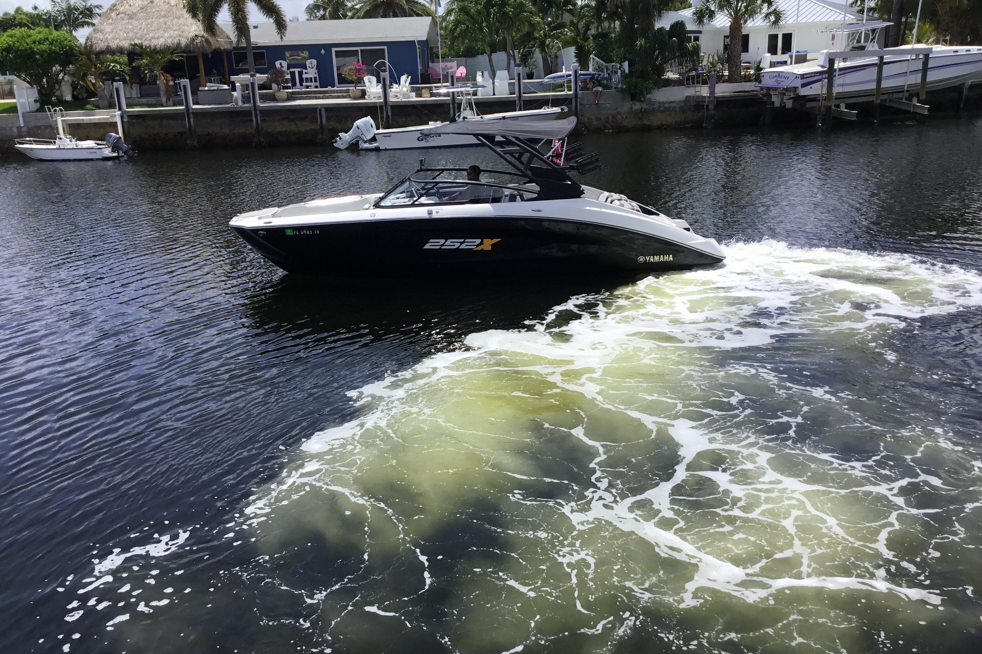 2023 Yamaha Boats 252XE cruising on a calm waterway near a dockside residence.