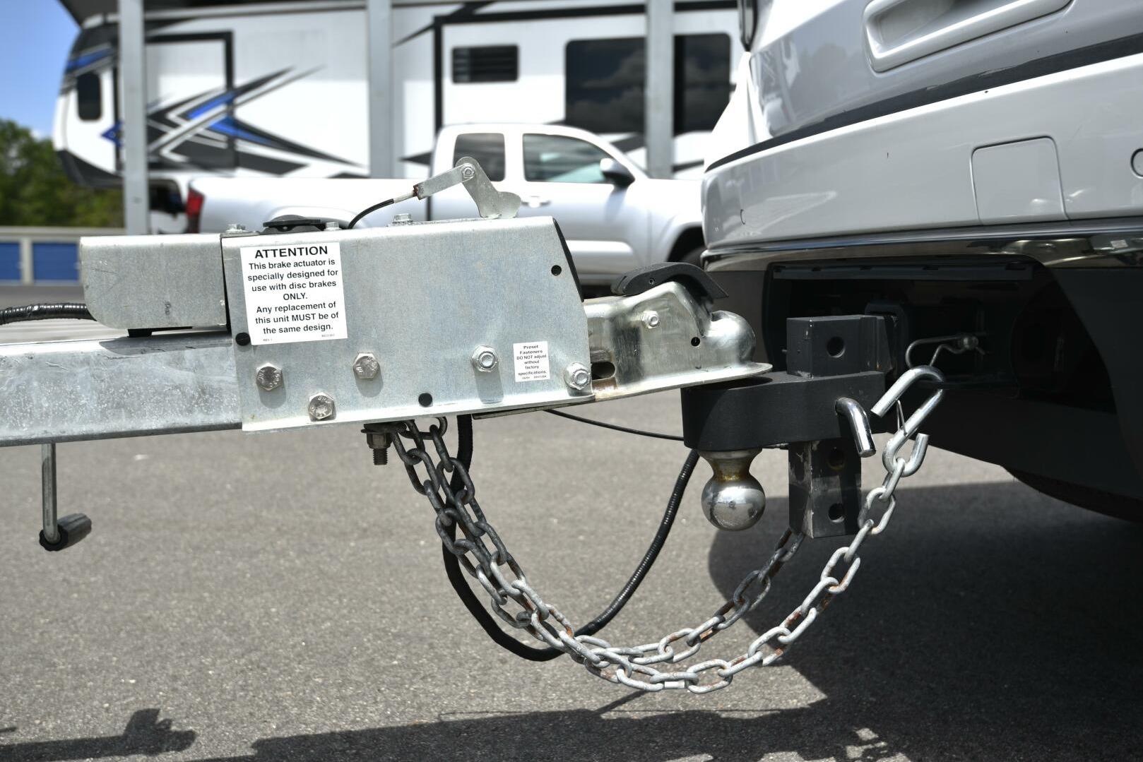 Trailer hitch connection on a vehicle, featuring a brake actuator and safety chains.