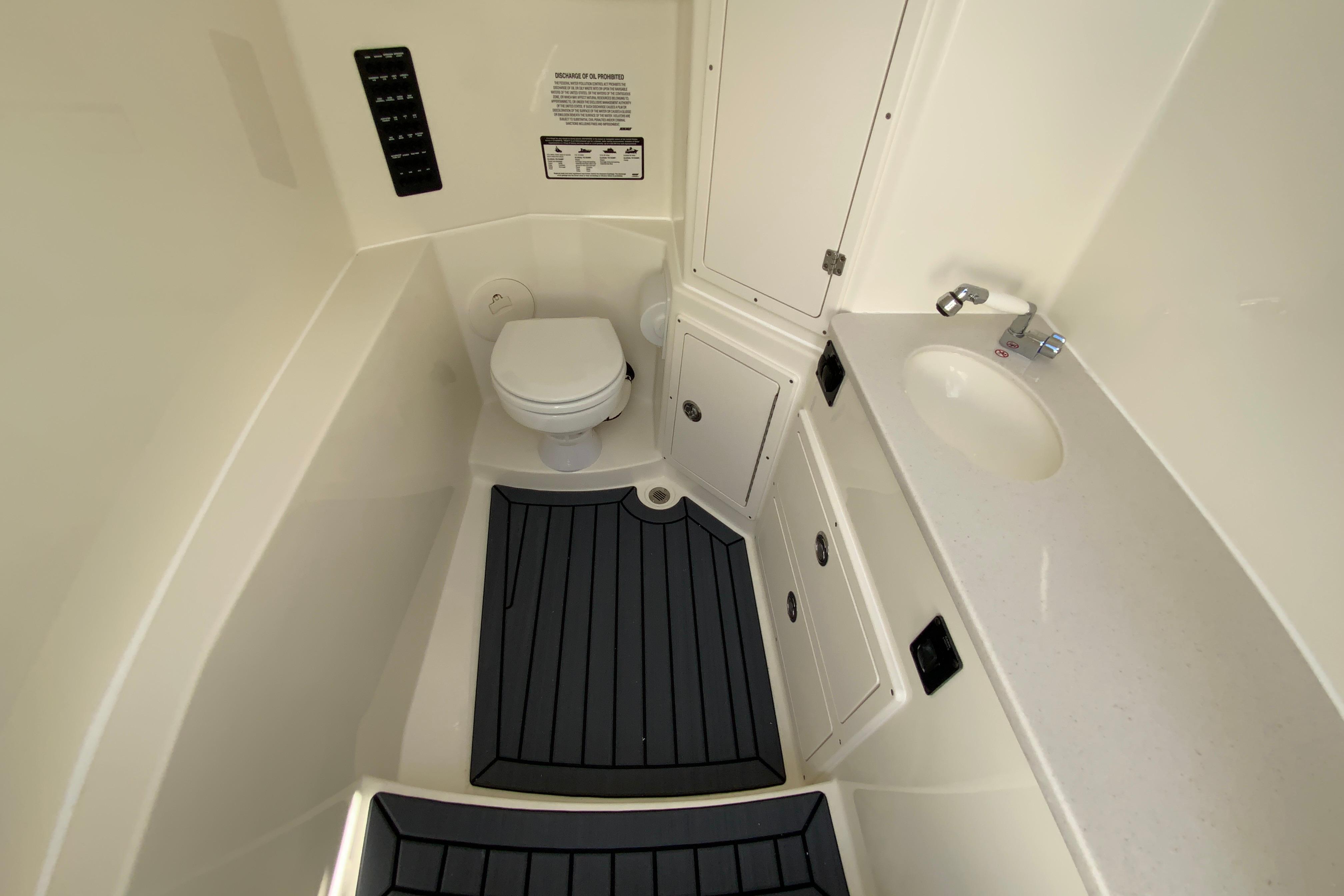 Interior of 2027 Cobia 320 Center Console boat, featuring a compact bathroom with toilet and sink.