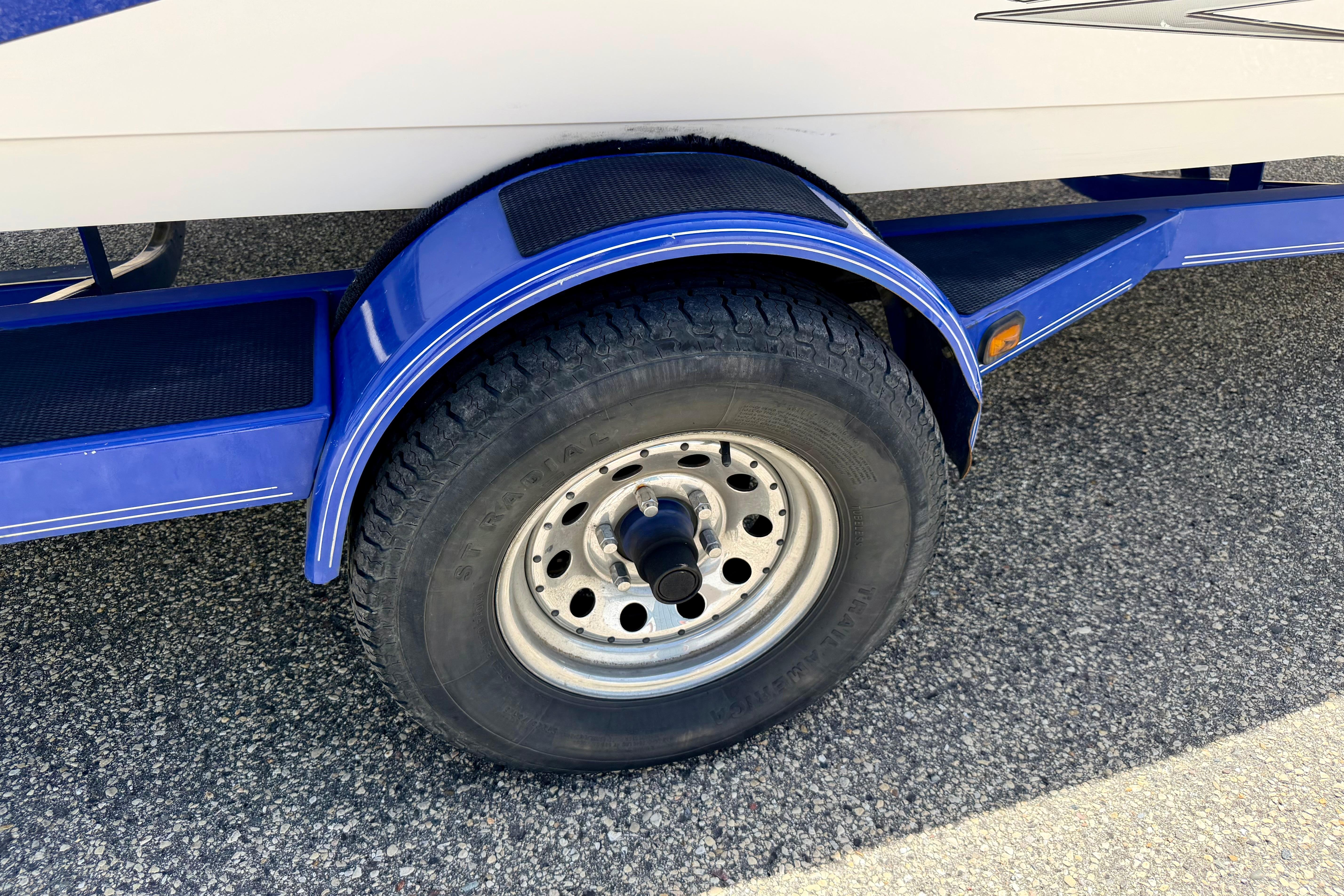 Blue trailer wheel of 2008 Moomba Outback V boat on asphalt surface.