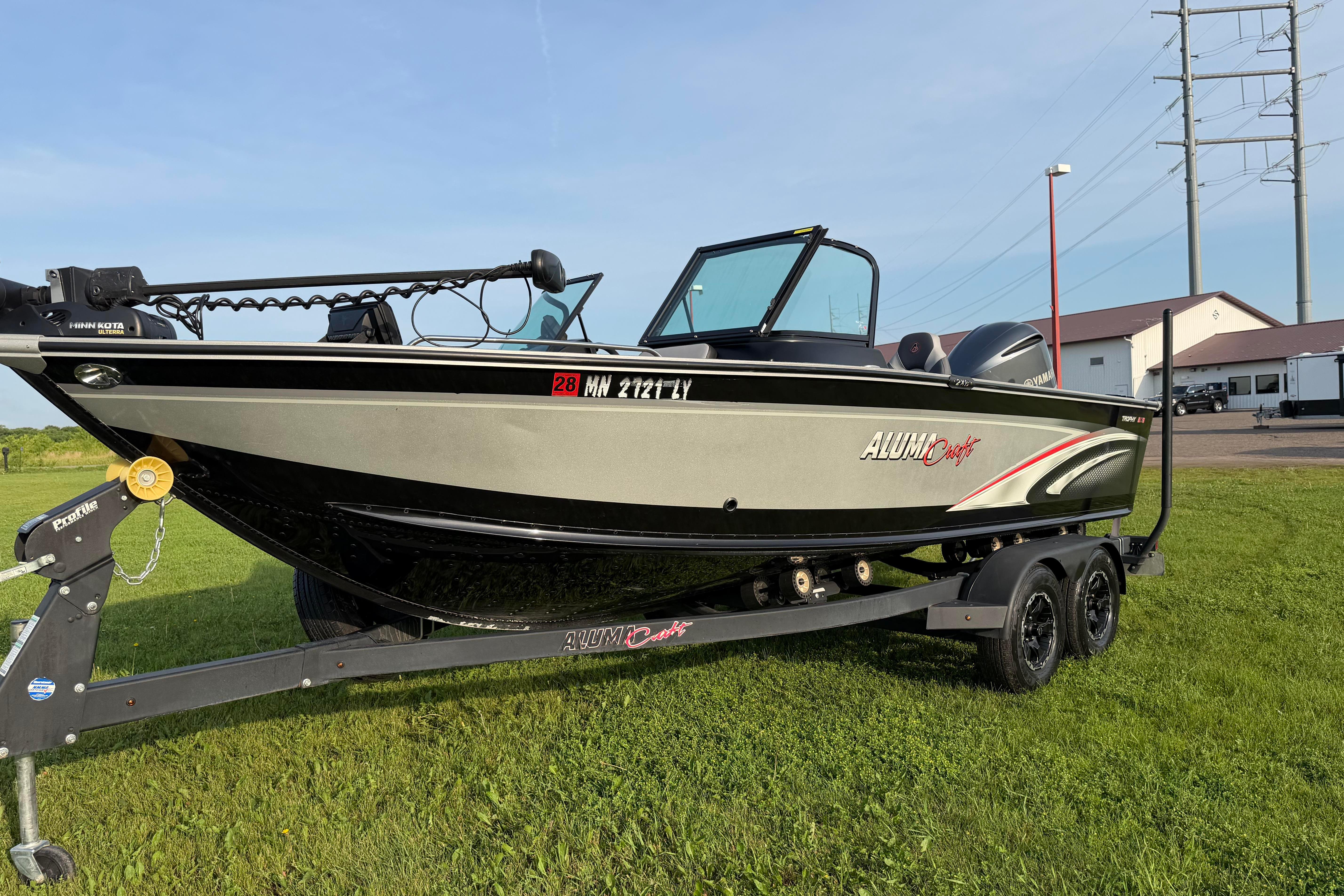 2019 Alumacraft Trophy 205 boat on trailer, parked on grass under clear sky.