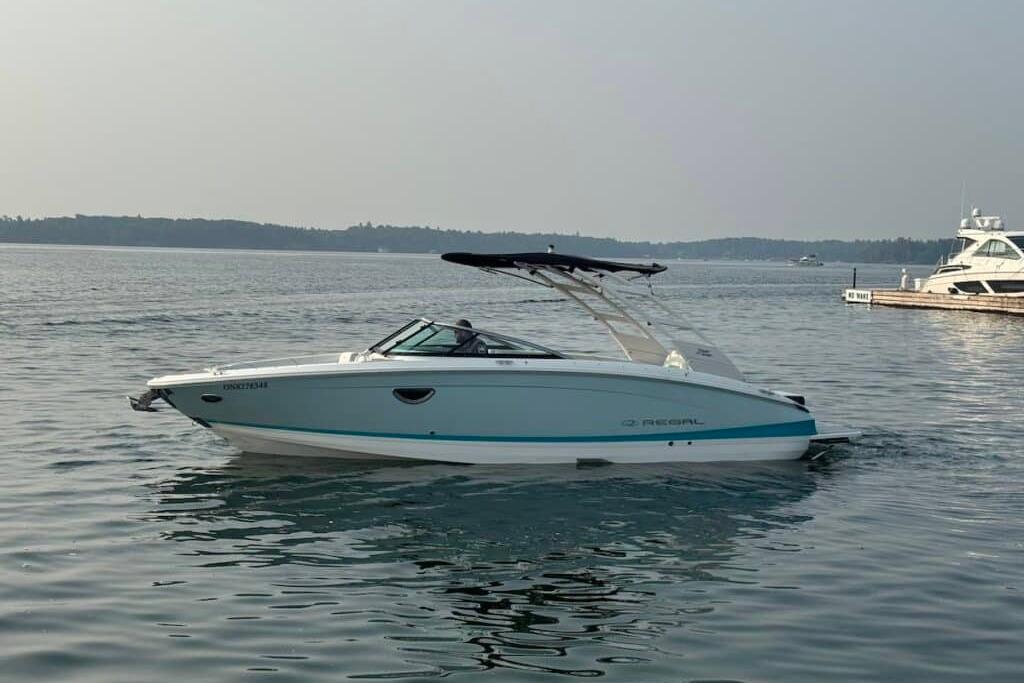 2022 Regal LS6 Surf boat cruising on a calm lake near a marina.