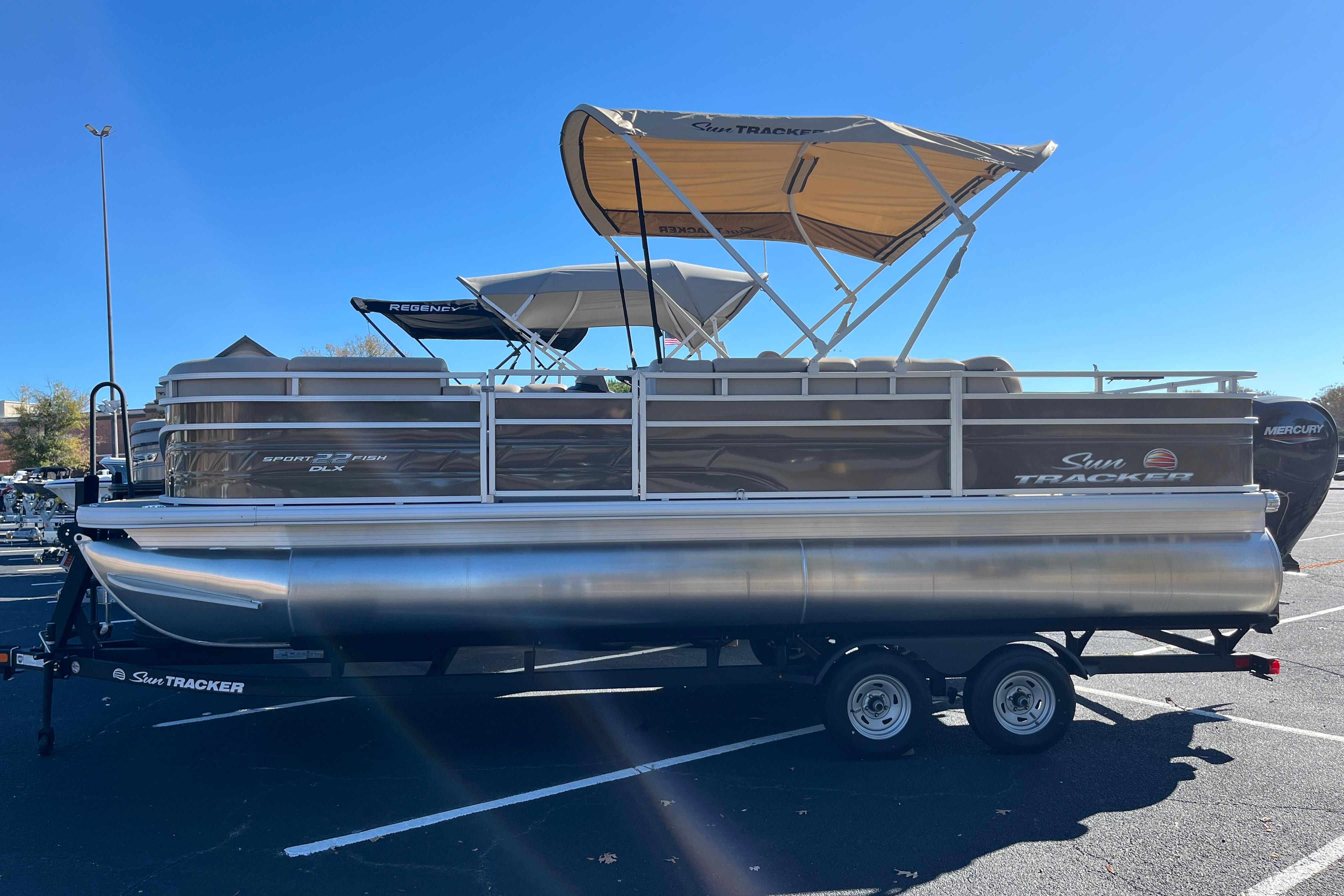 2025 Sun Tracker SportFish 22 DLX pontoon boat with canopy, parked on a trailer.