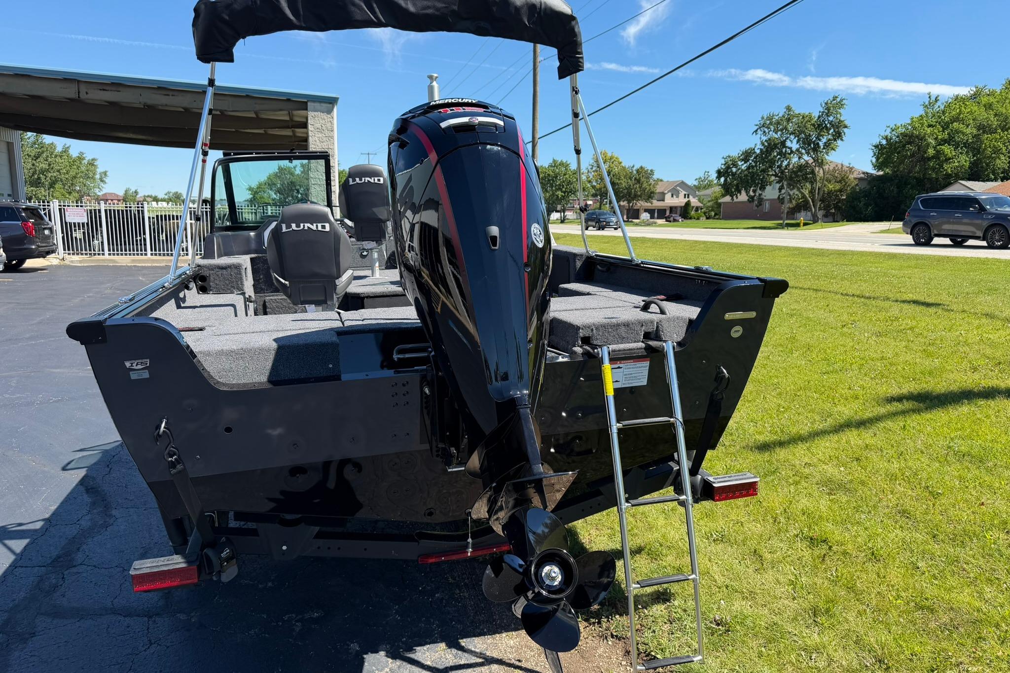 2027 Lund 1775 Impact XS Sport boat with outboard motor and ladder on grassy area.