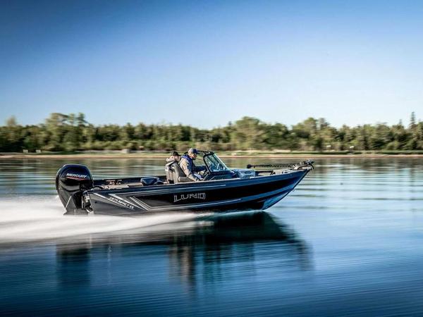 2026 Lund 1875 Impact XS boat speeding on a calm lake with trees in the background.
