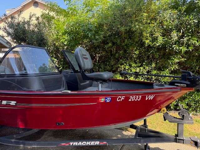 A red Tracker boat, model PGV16WT 16, is on a trailer outdoors.