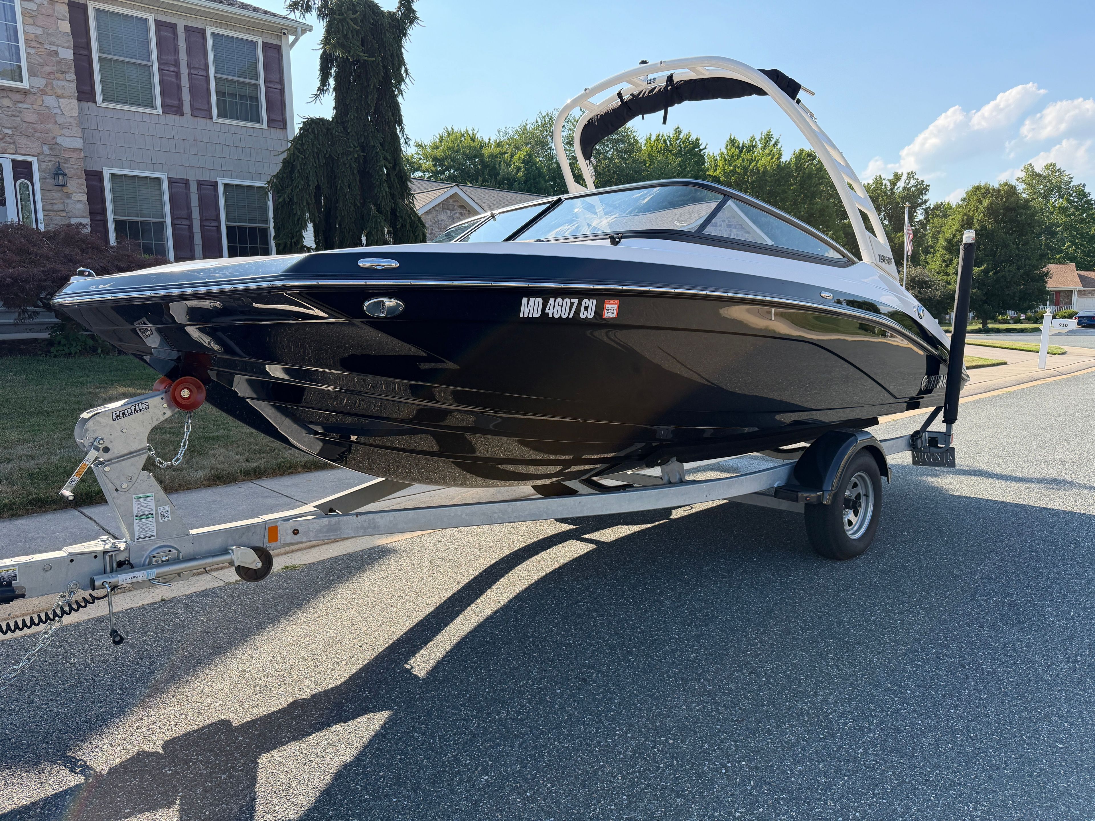 A 2023 Yamaha 195S boat on a trailer, parked on a street in front of a house.