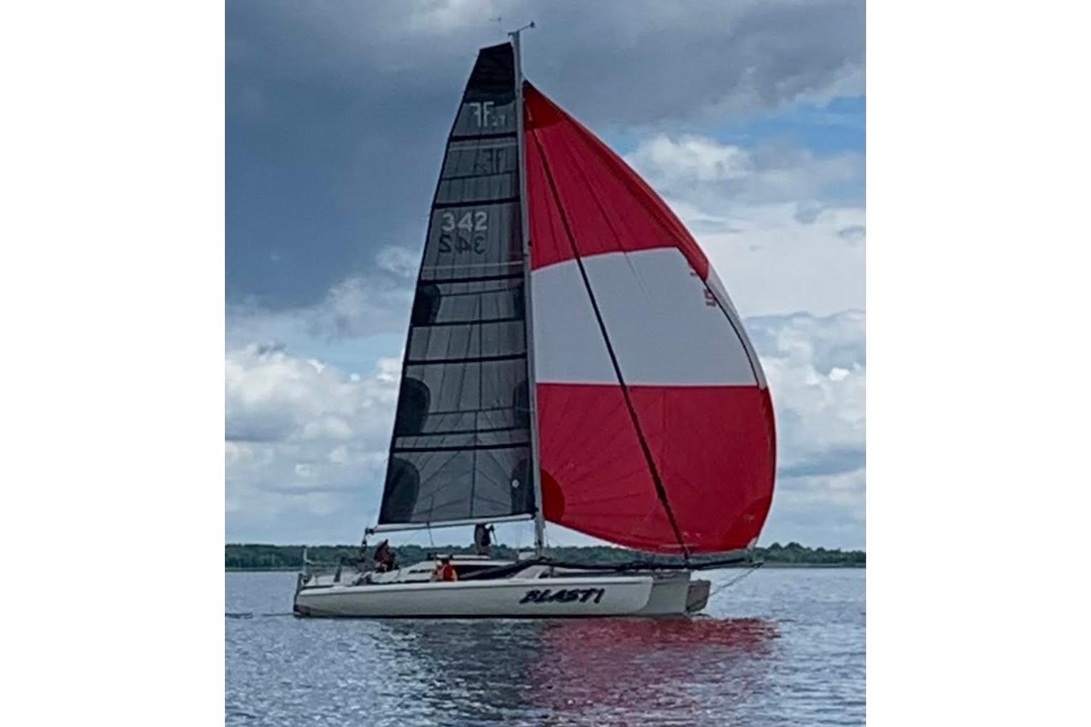 Sailing Corsair F-27 trimaran with red and white spinnaker on a calm lake.